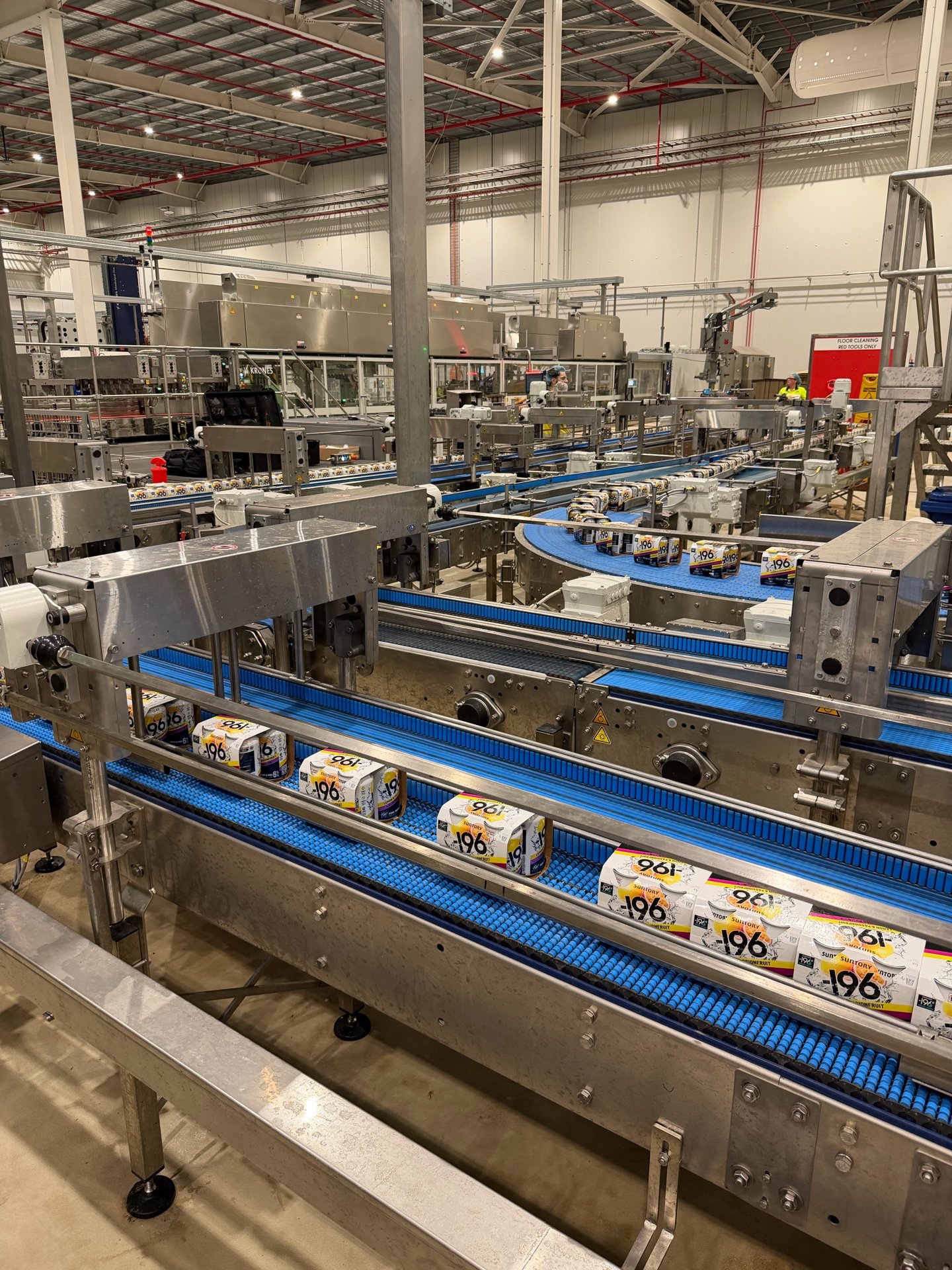 A conveyor belt in a factory transports cartons of drinks through an industrial production line with workers supervising.