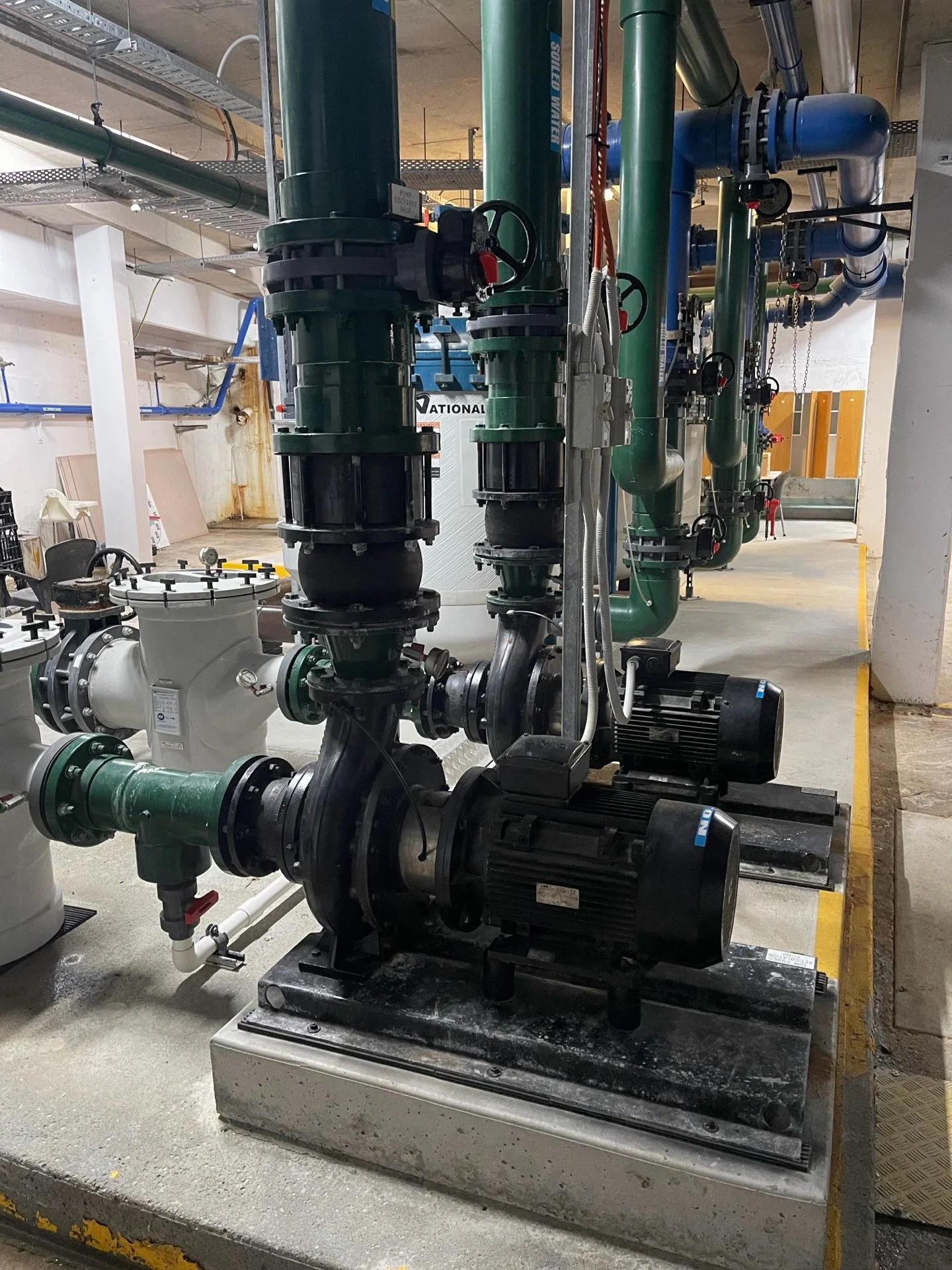 Industrial pump system with green pipes, black motors, and gauges in a utility room.