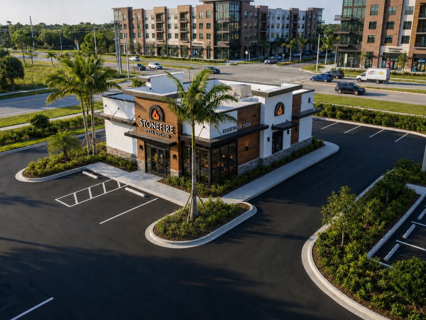 A modern, empty parking lot in front of a restaurant called Stonefire Pizza Kitchen, with palm trees and a multi-story residential building in the background.