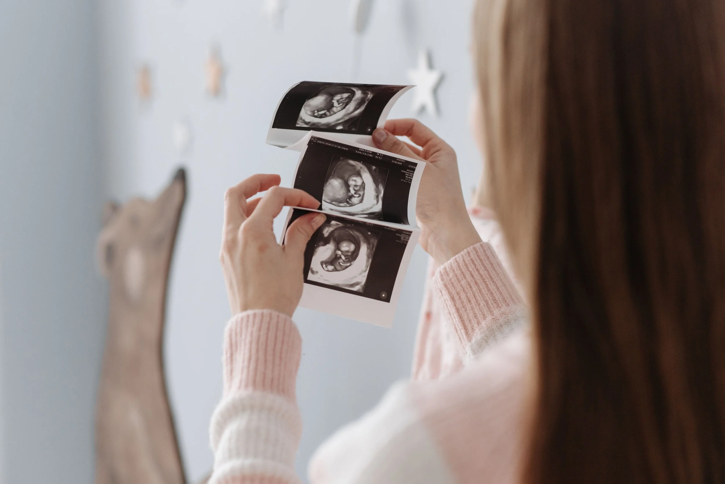 A person holding ultrasound pictures of a fetus.