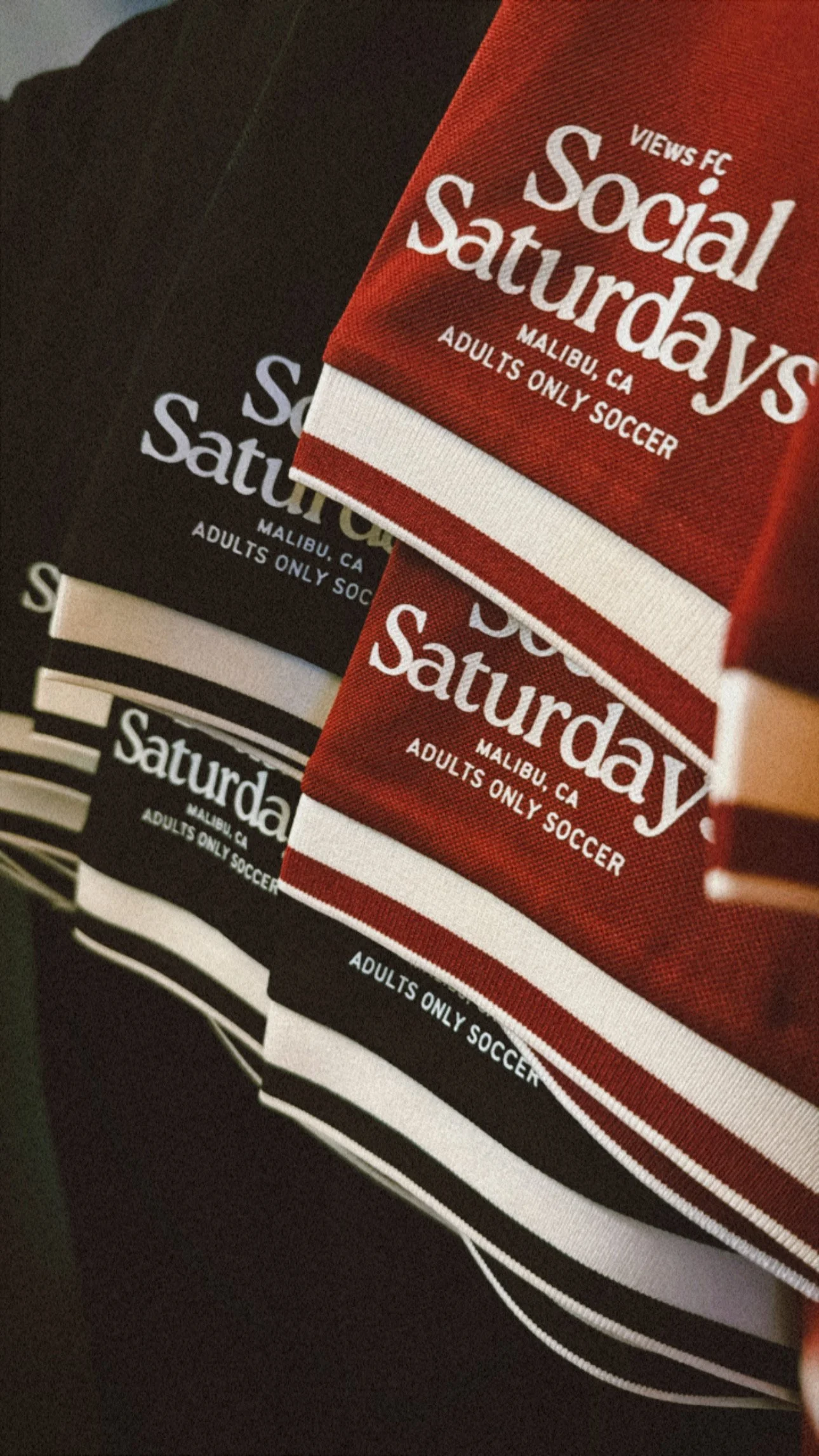 A stack of t-shirts with social Saturday design in red, black, and white, promoting adult adult soccer in Malibu, California.