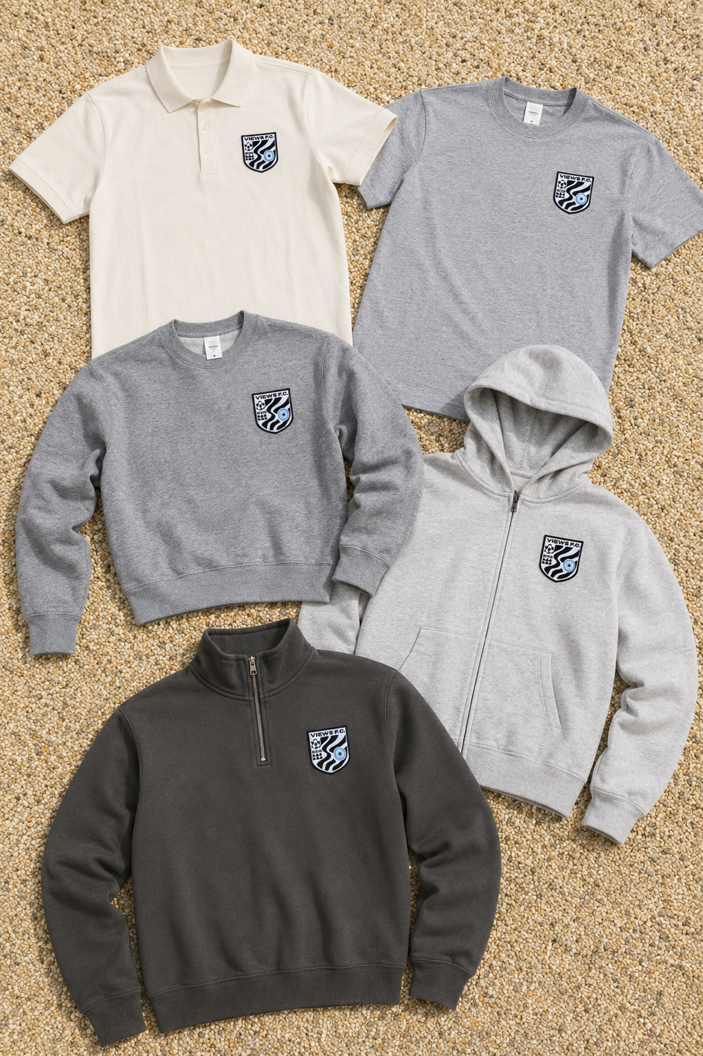 Collection of four casual clothing items with a sports team logo, laid out on a sandy surface. The items include a white polo shirt, a grey t-shirt, a light grey zip-up hoodie, and a dark grey quarter-zip sweatshirt.