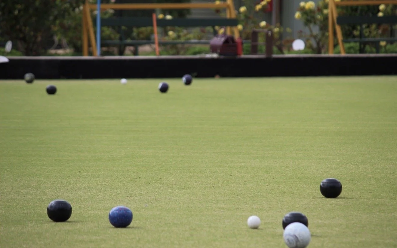 A lawn bowl green with several black, white, and colored balls scattered across it.