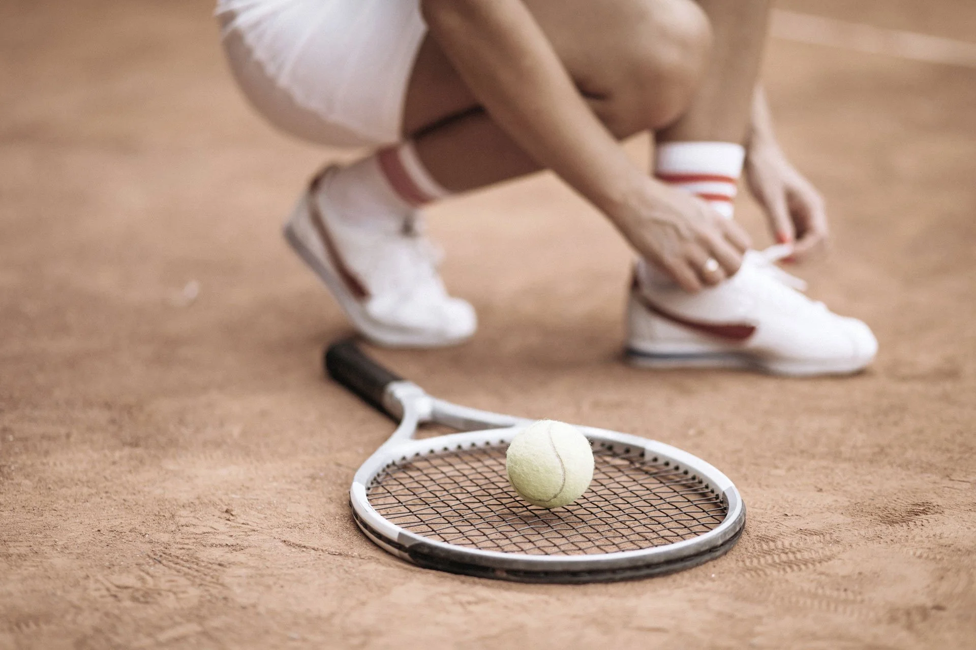 Tennisspielerin auf Sandplatz mit Tennisschläger und Ball.