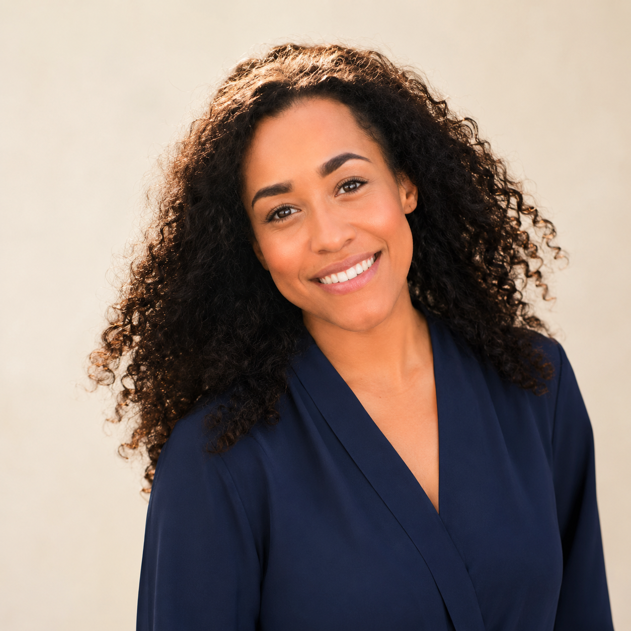 Headshot of a smiling woman with curly dark hair wearing a dark blue top against a neutral background.