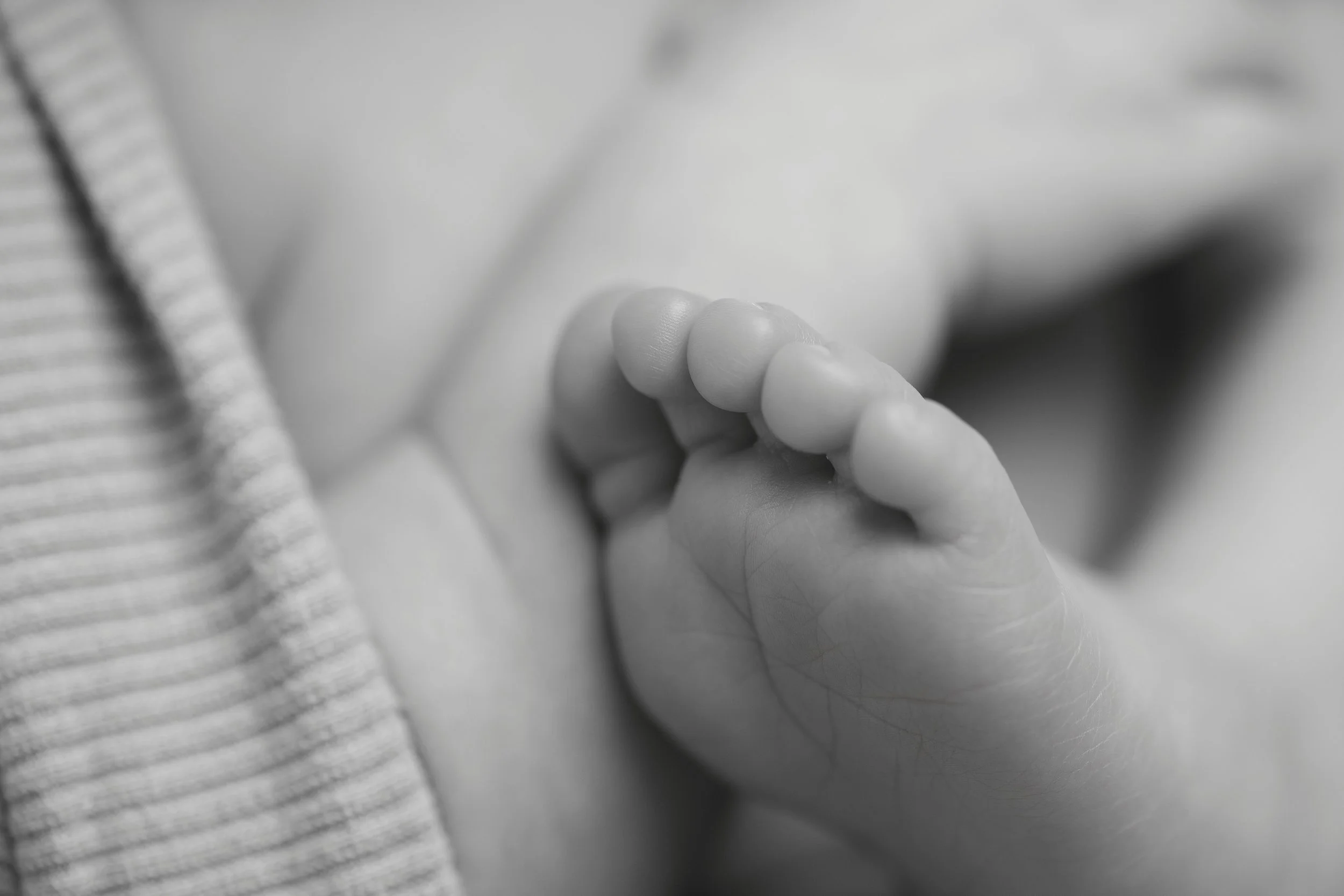 Close-up of a person holding a tiny baby finger, with blurred background and striped fabric on the side.