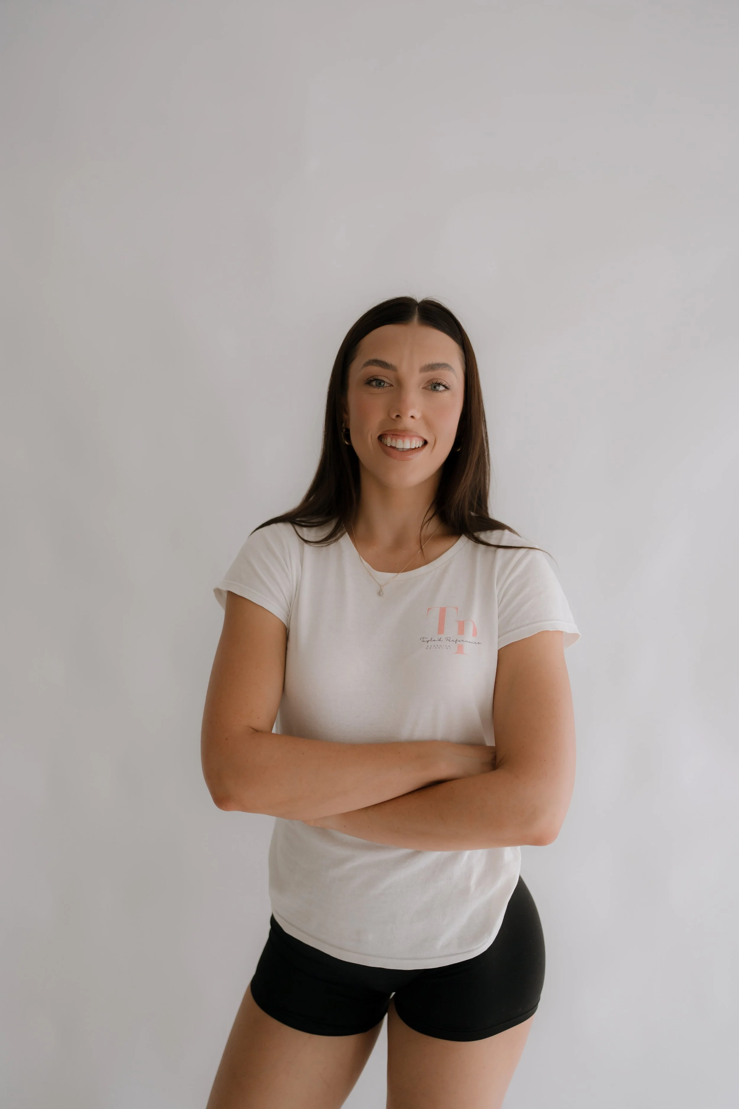 Exercise Physiologist, crossing her arms and smiling in front of a plain white wall.