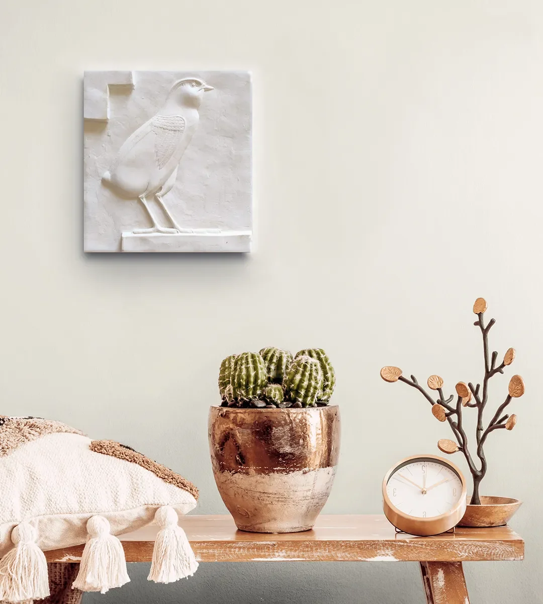Decorative wall art of a white bird, potted cactus, wooden leaf tree sculpture, and a clock on a wooden table.