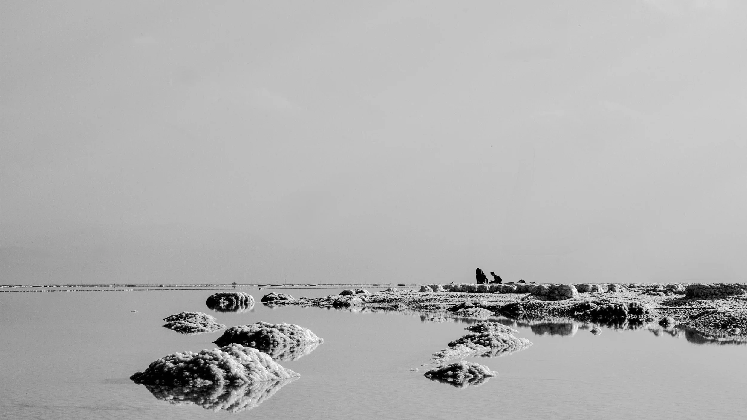 Black-and-white salt formations spread across shallow water with two distant figures near the horizon.