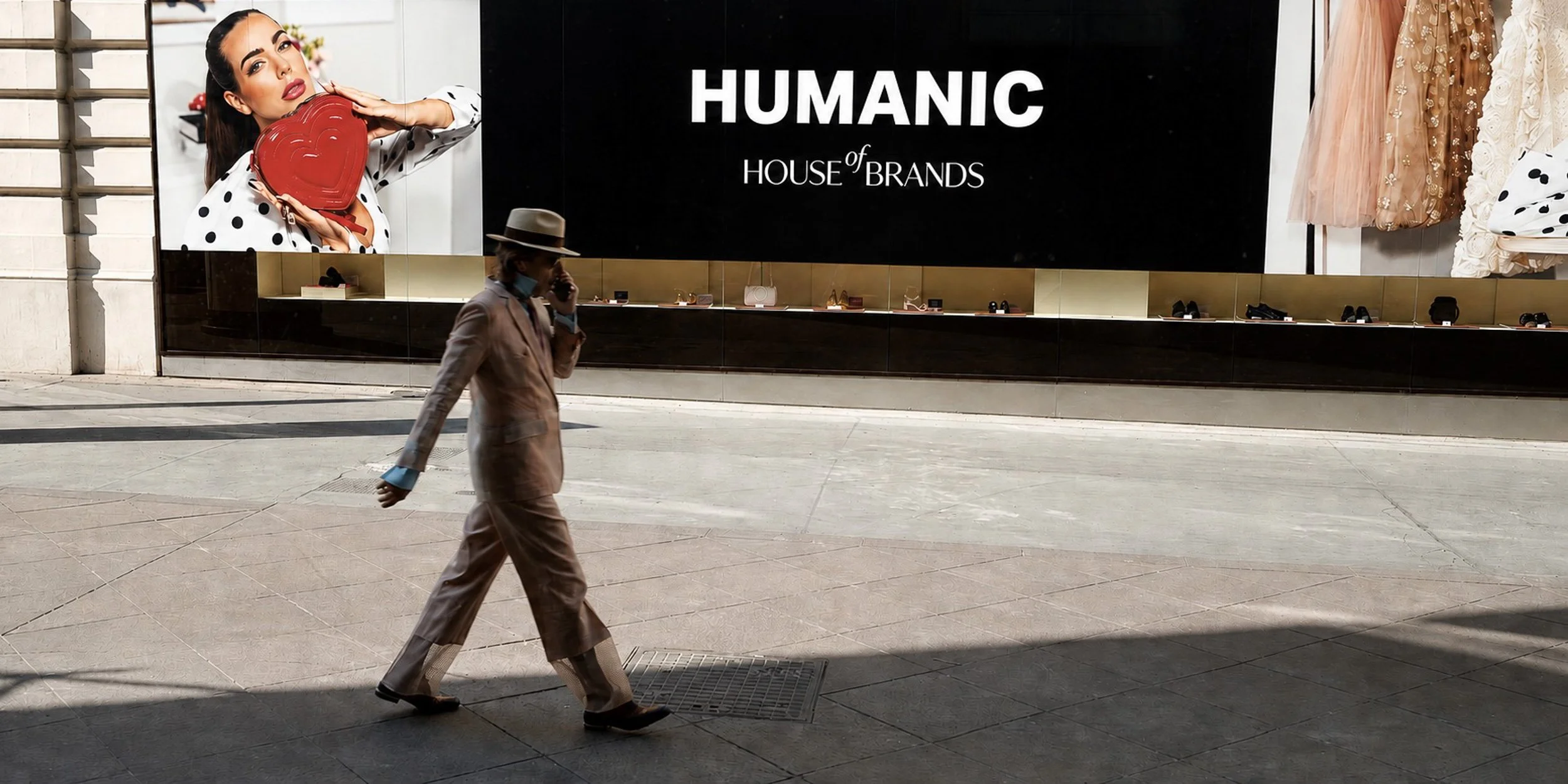 Man in a brown suit and hat walks past a billboard of a woman holding a red heart-shaped object.