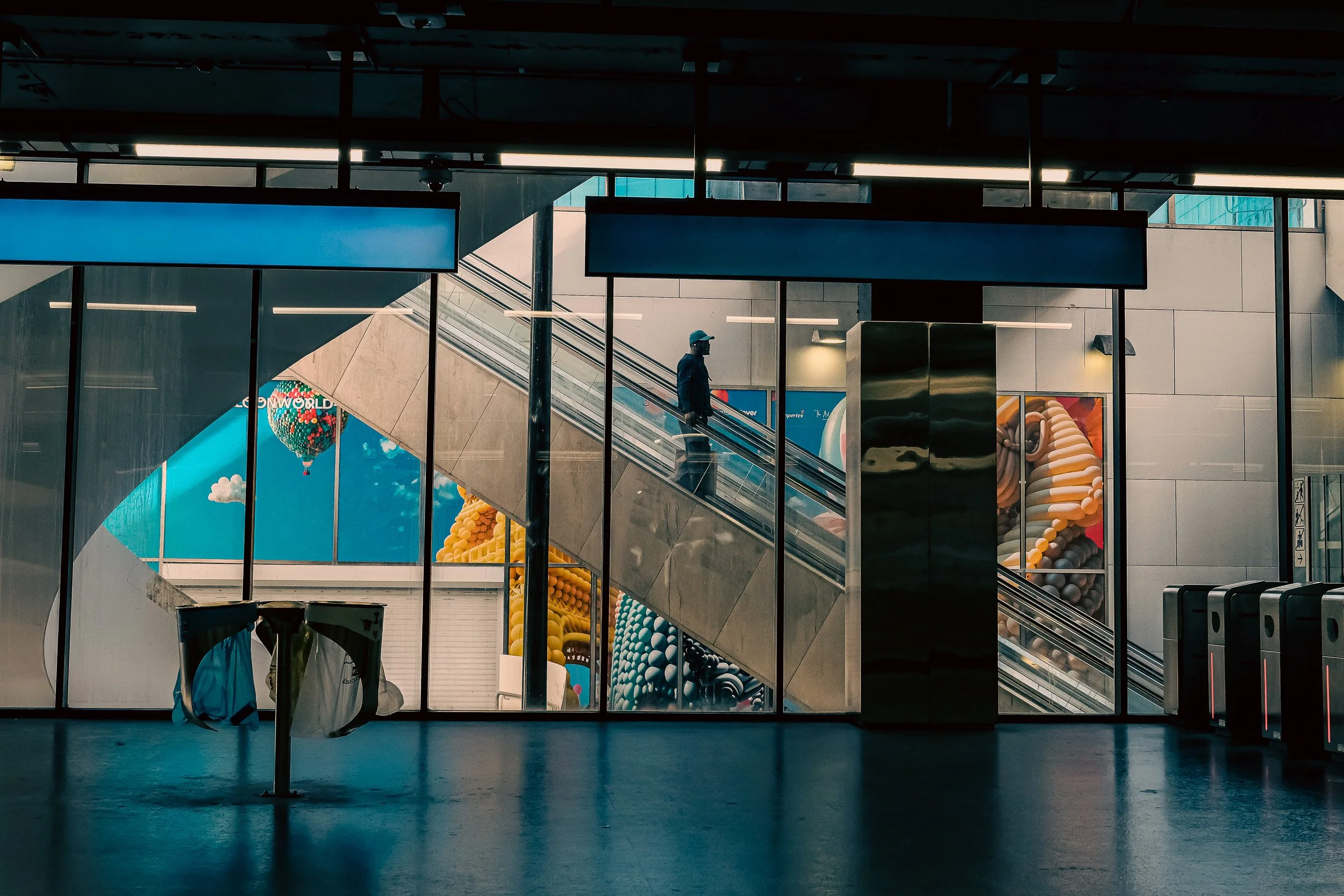 Lone passenger rides an escalator behind glass walls and blue station signs.