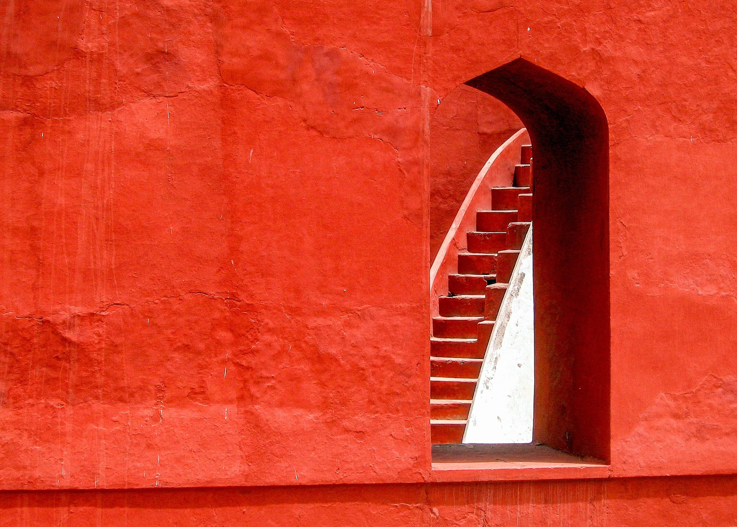 Narrow opening in a vivid red wall revealing a white staircase.