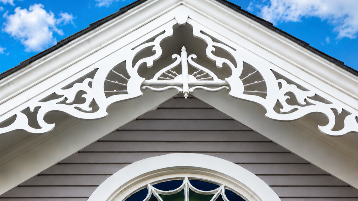 Close-up of the decorative white trim and gable of a house with a blue sky background.