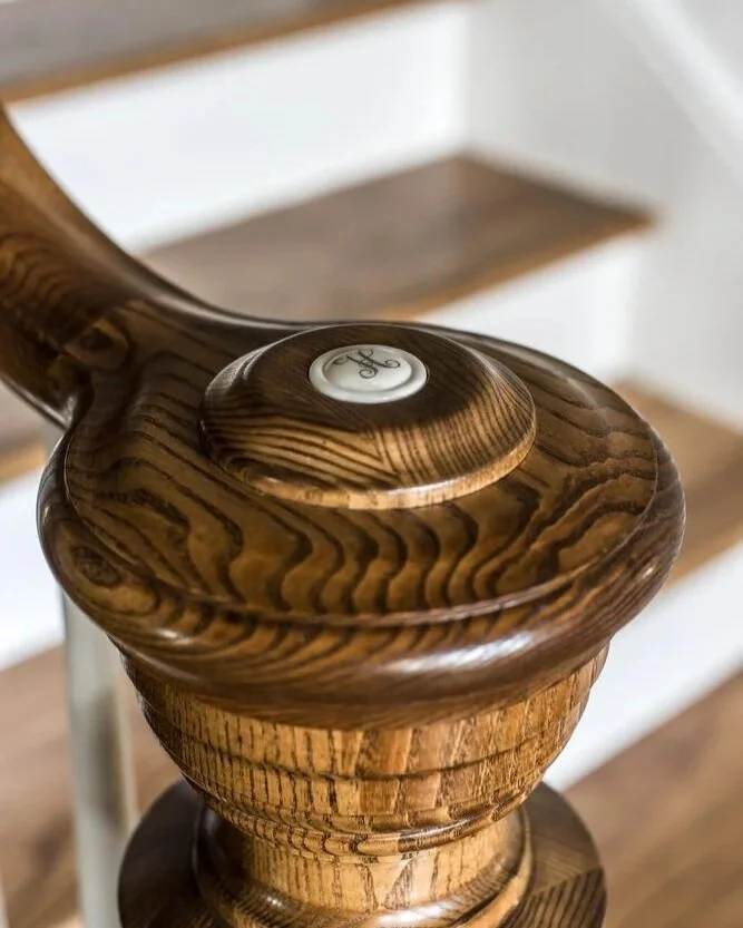 Close-up of a wooden banister post with a white circular cap engraved with the letter 'H'.