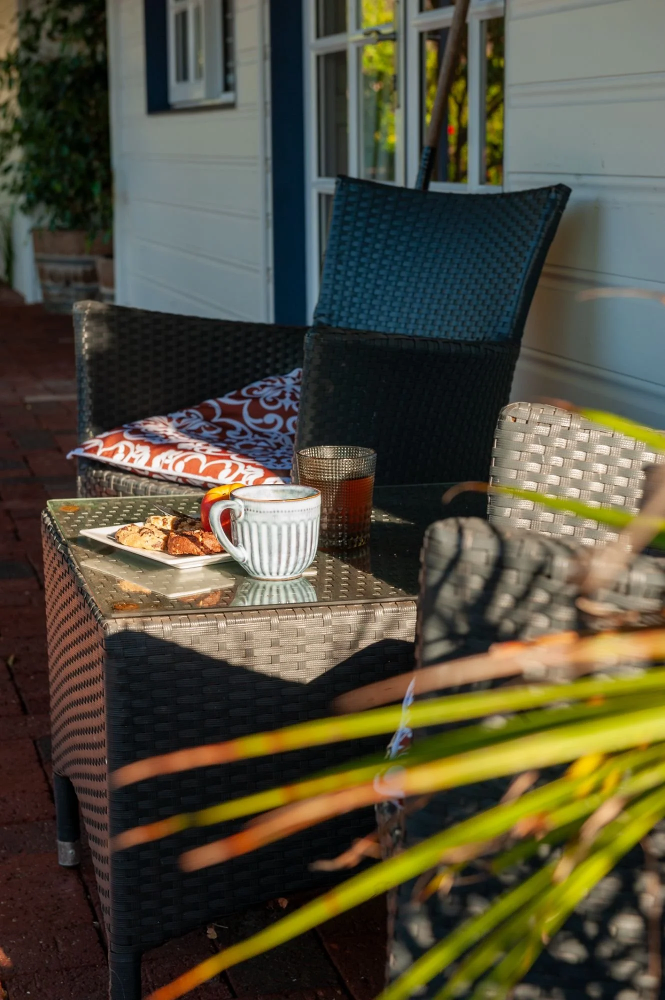 Outdoor patio scene with a wicker chair, a small table holding a mug, a glass, and cookies.