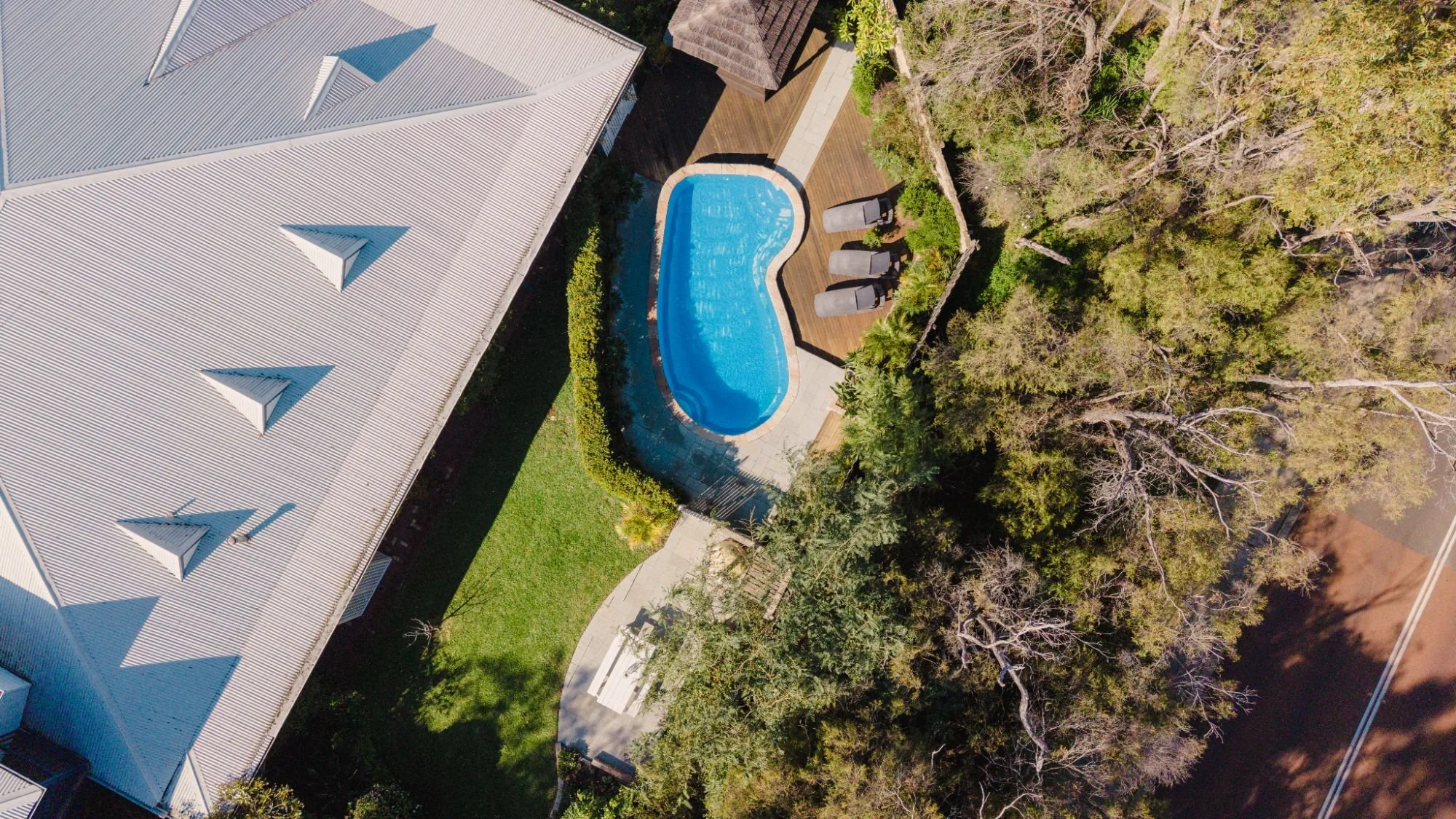 Aerial view of Lanterns Retreat backyard with swimming pool, surrounded by a wooden deck and lounge chairs.