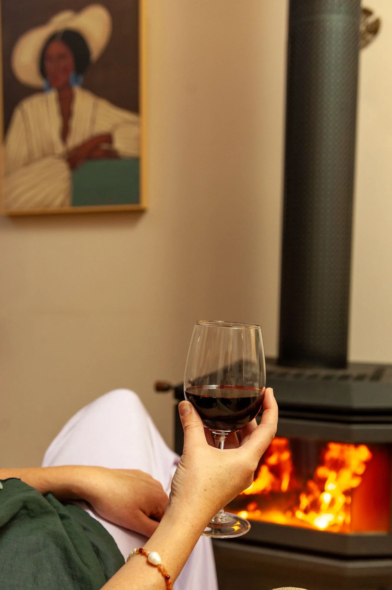 Person sitting near a fireplace with a glass of red wine in hand at Lanterns Retreat
