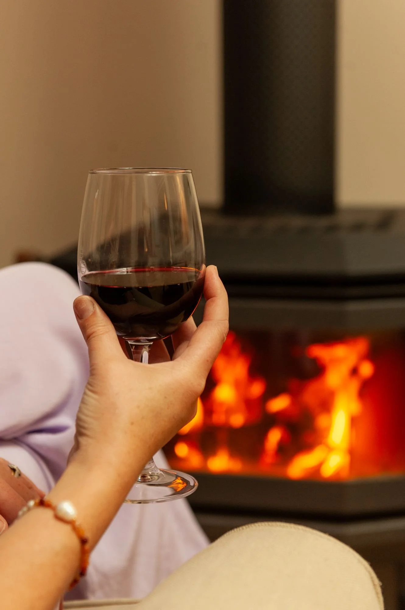 Person holding a glass of red wine in front of a lit fireplace.