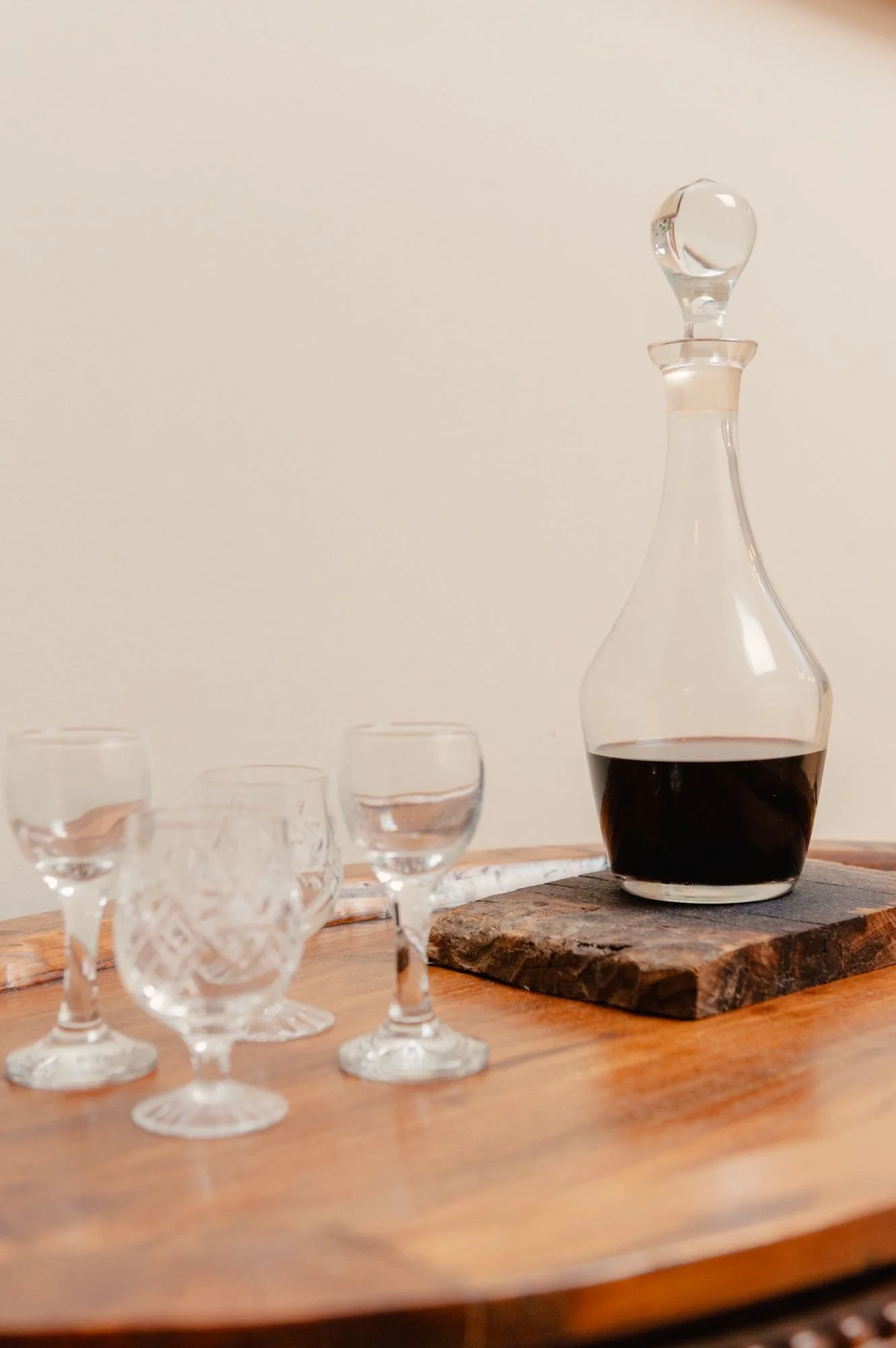 A glass decanter filled with red wine on a wooden table, surrounded by several glasses.