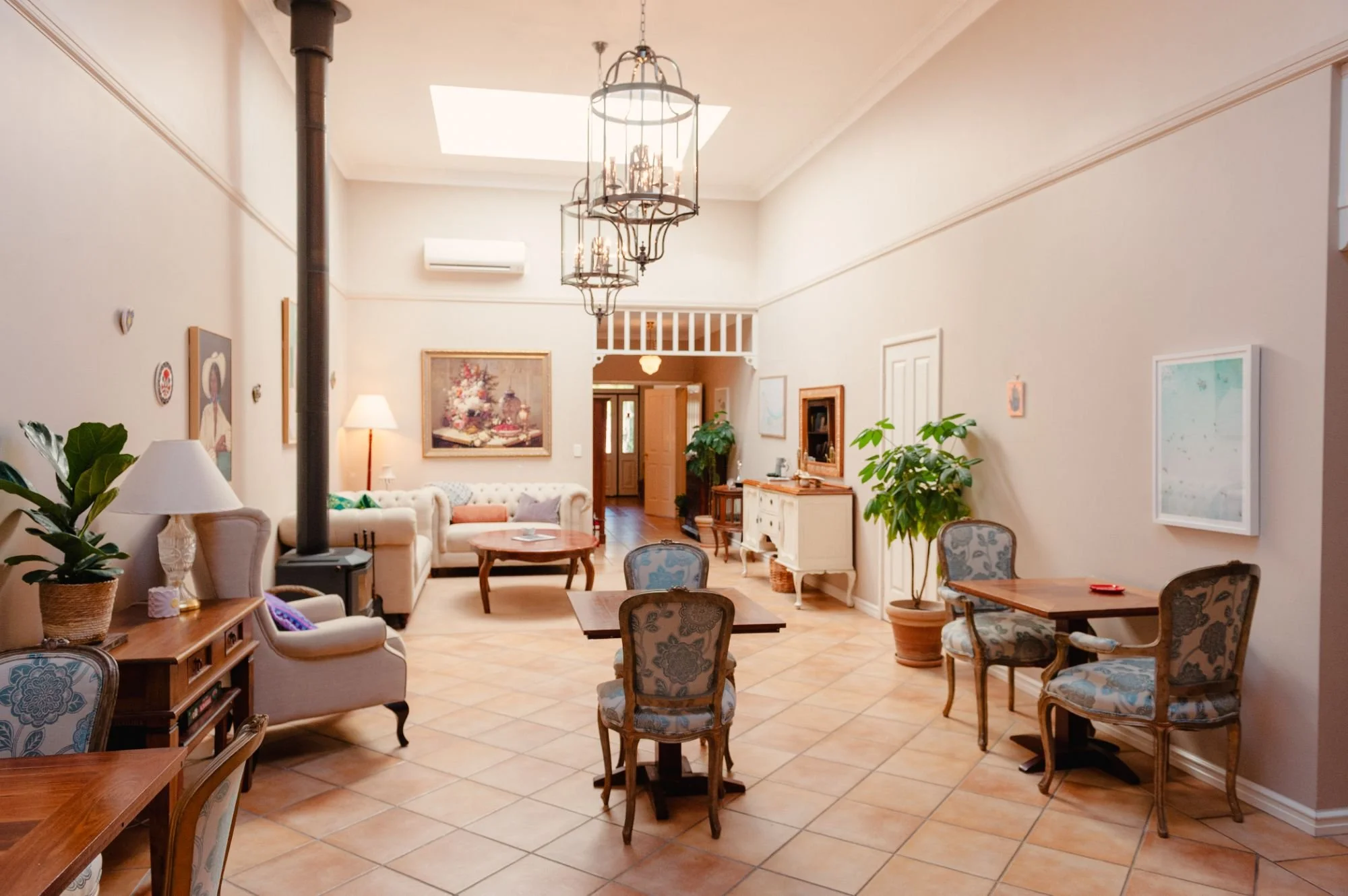 Lanterns Retreat living room with wooden furniture, patterned chairs, a white sofa, wall art, plants, and a skylight.