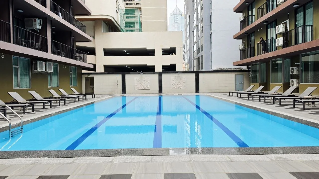 Empty outdoor swimming pool in a high-rise building complex surrounded by lounge chairs and balconies.
