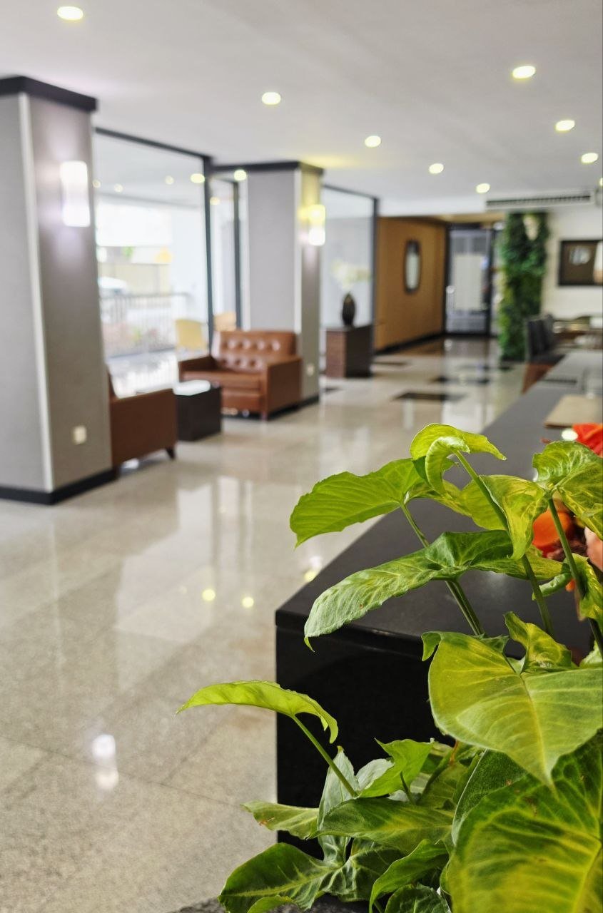 The lobby of a modern hotel, seating area with leather chairs, large windows, and polished tile flooring.