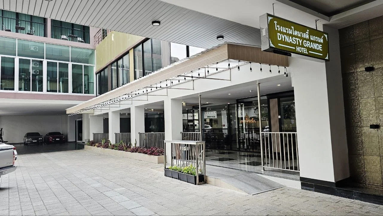 Exterior view of Dynasty Grande Hotel with a sign and a parking area, modern architecture with glass windows and outdoor lighting.
