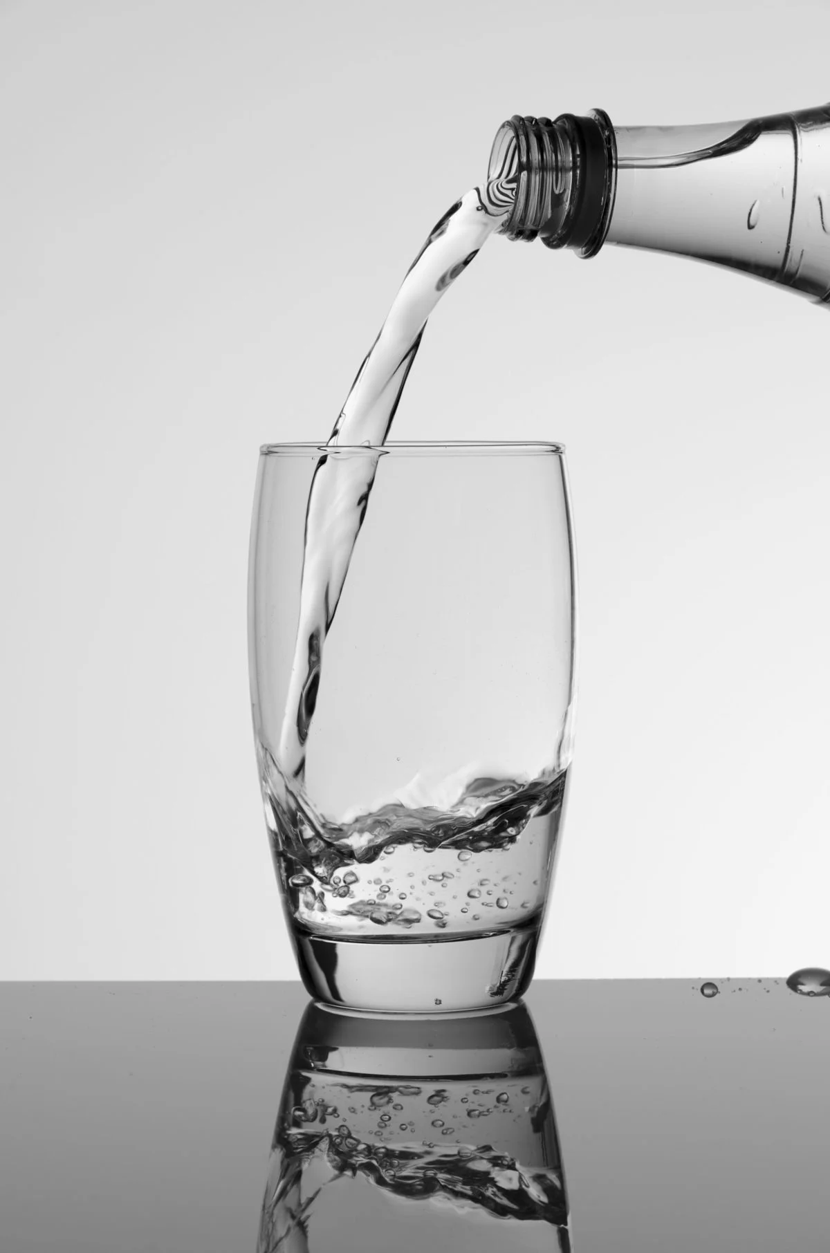 Black and white photo of water being poured from a bottle into a glass, with splashes and bubbles visible.