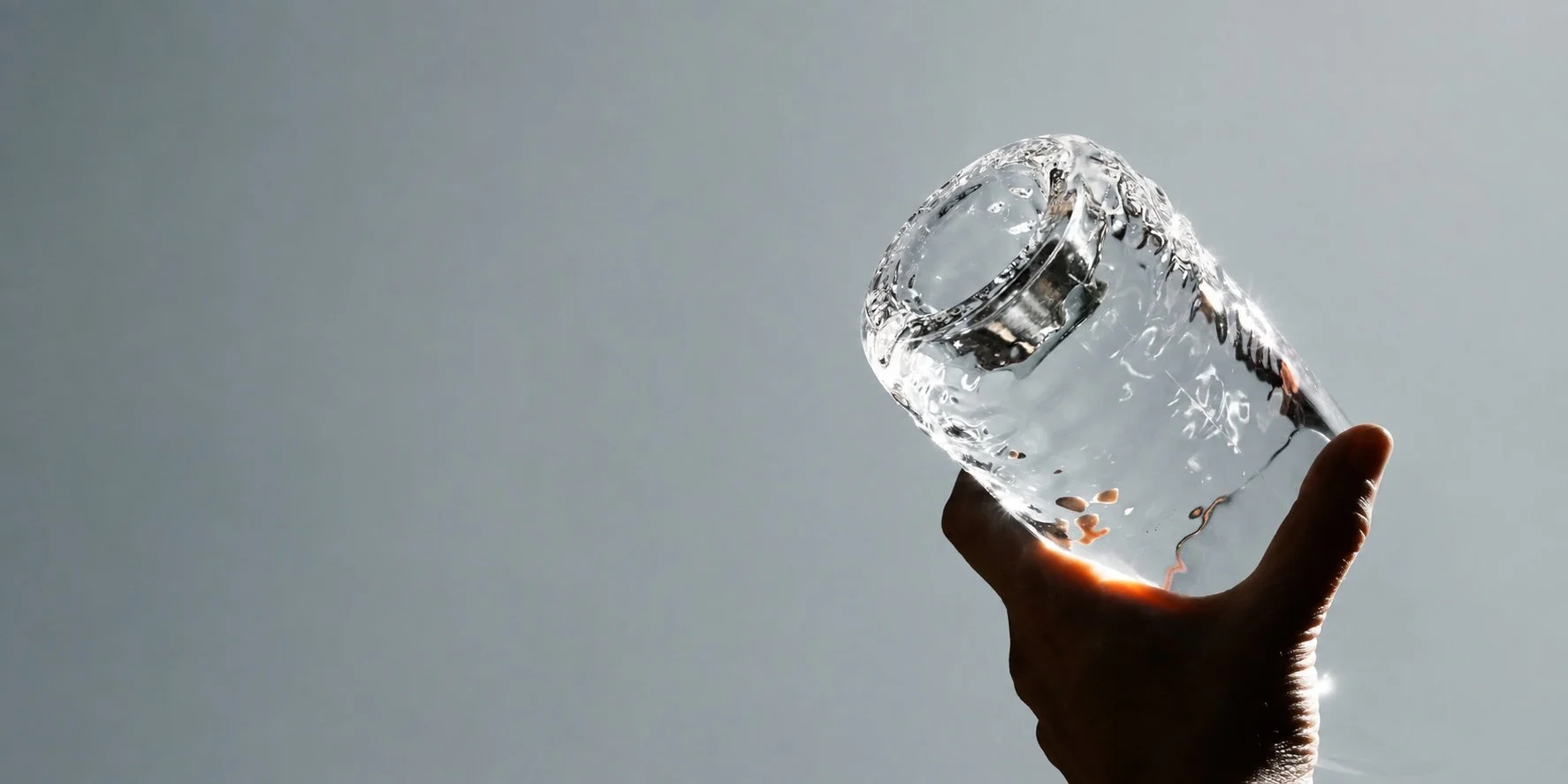 A hand holding a glass of water against a bright background.