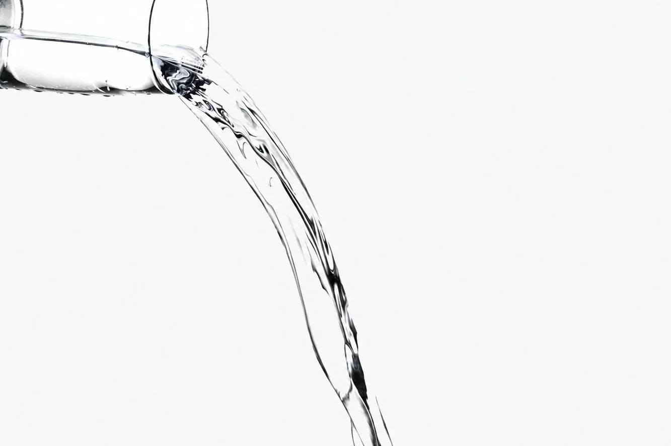 Flowing water pouring from a glass against a plain white background.