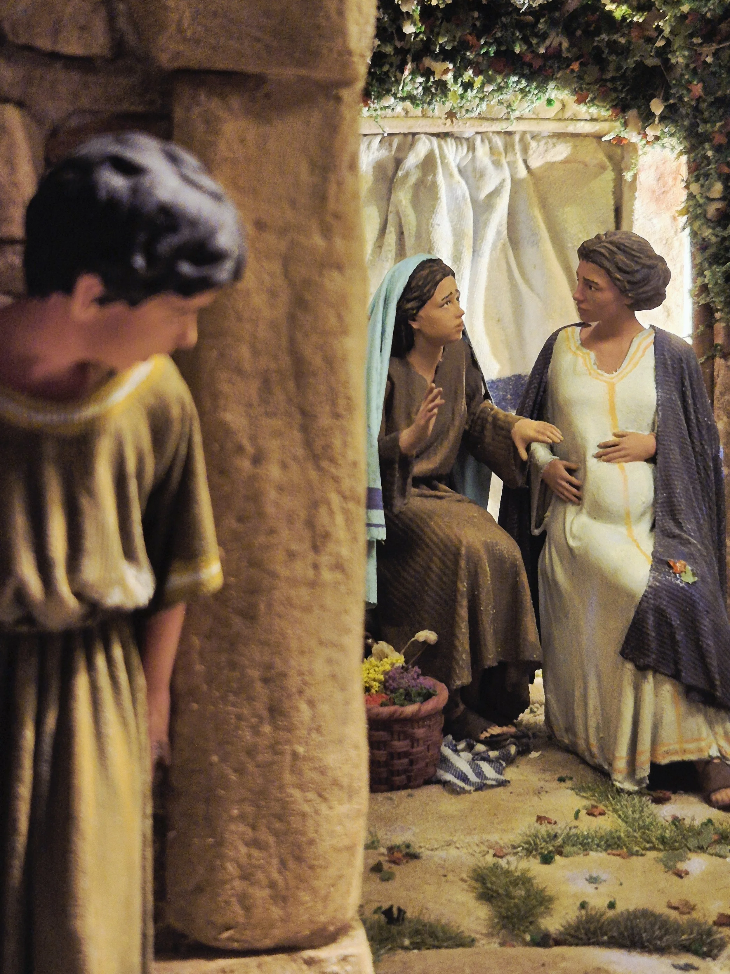 Statue di Gesù Cristo e una donna, forse Maria, in un ambiente che sembra una grotta o un uscio, decorato con fiori e piante.