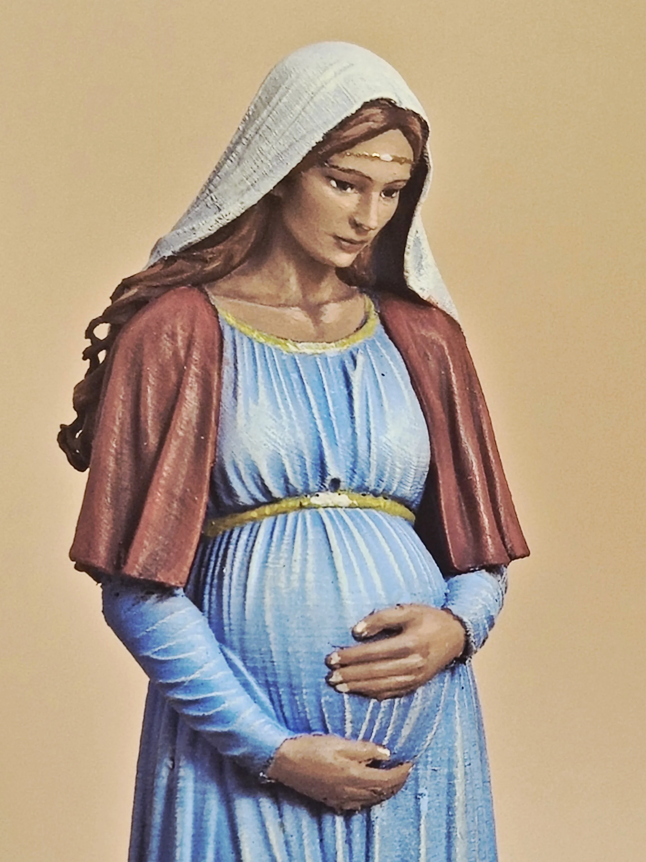 Statua di Vergine Maria incinta in abiti blu, che sostiene il ventre con le mani.