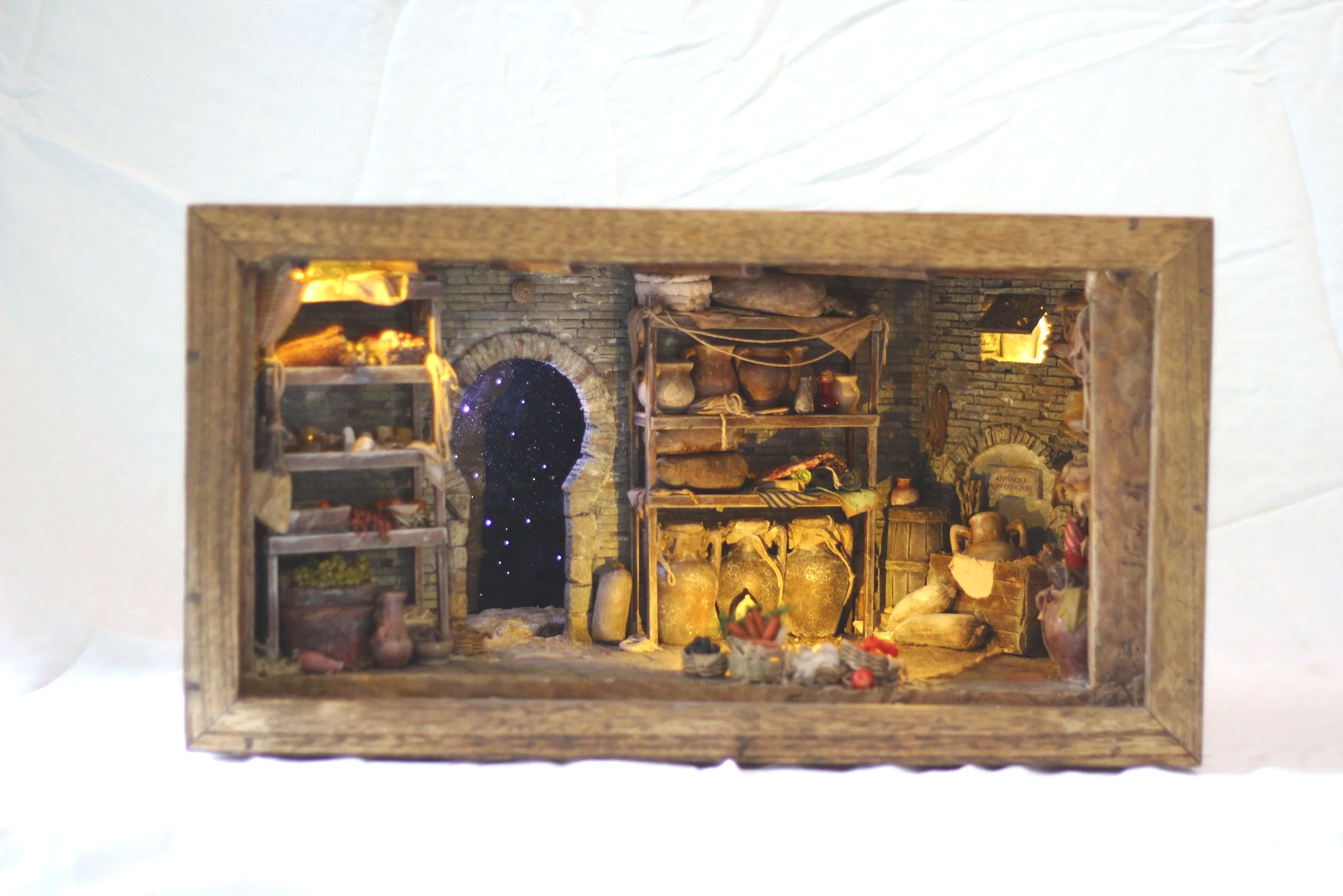 Interno di una stanza rustica con pareti in pietra, scaffali di legno pieni di recipienti di terracotta e oggetti decorativi, un camino in pietra e vari strumenti e decorazioni antiche.