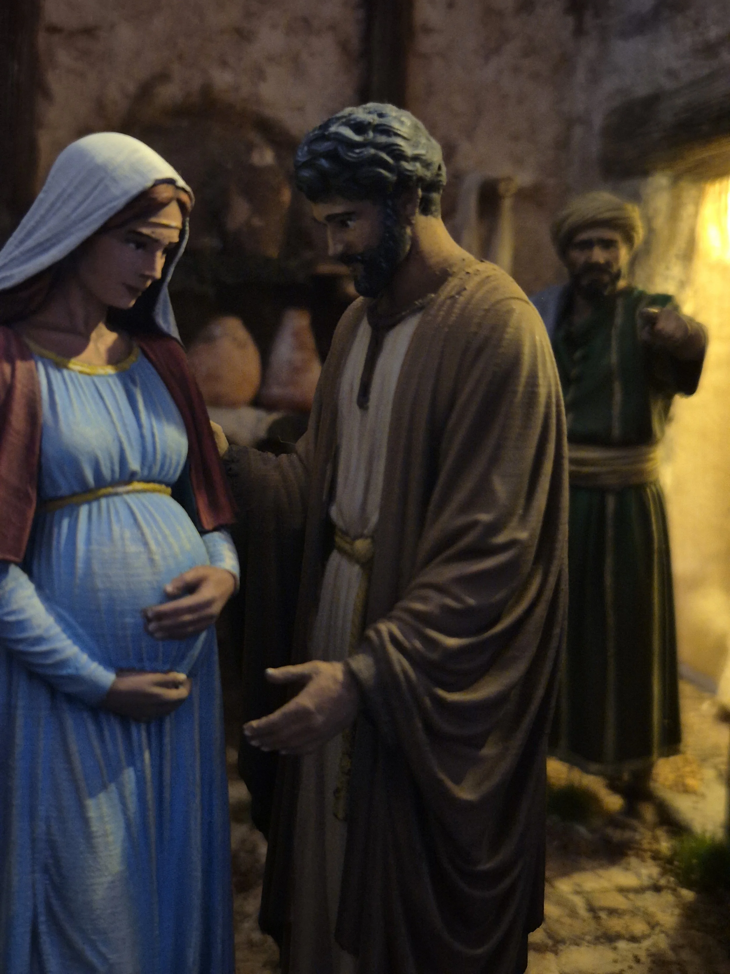 Statua di Maria e Giuseppe alla ricerca dell'alloggio. Un albergatore in un ambiente interno con luci calde.