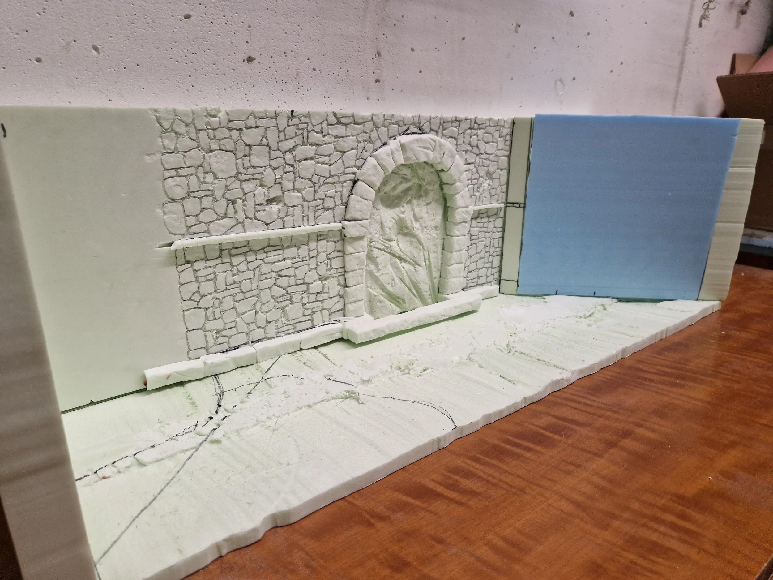 Modello di parete con mosaico in pietra bianca, arco e porta in miniscaola. Base in gesso con disegni e tracce di progettazione.