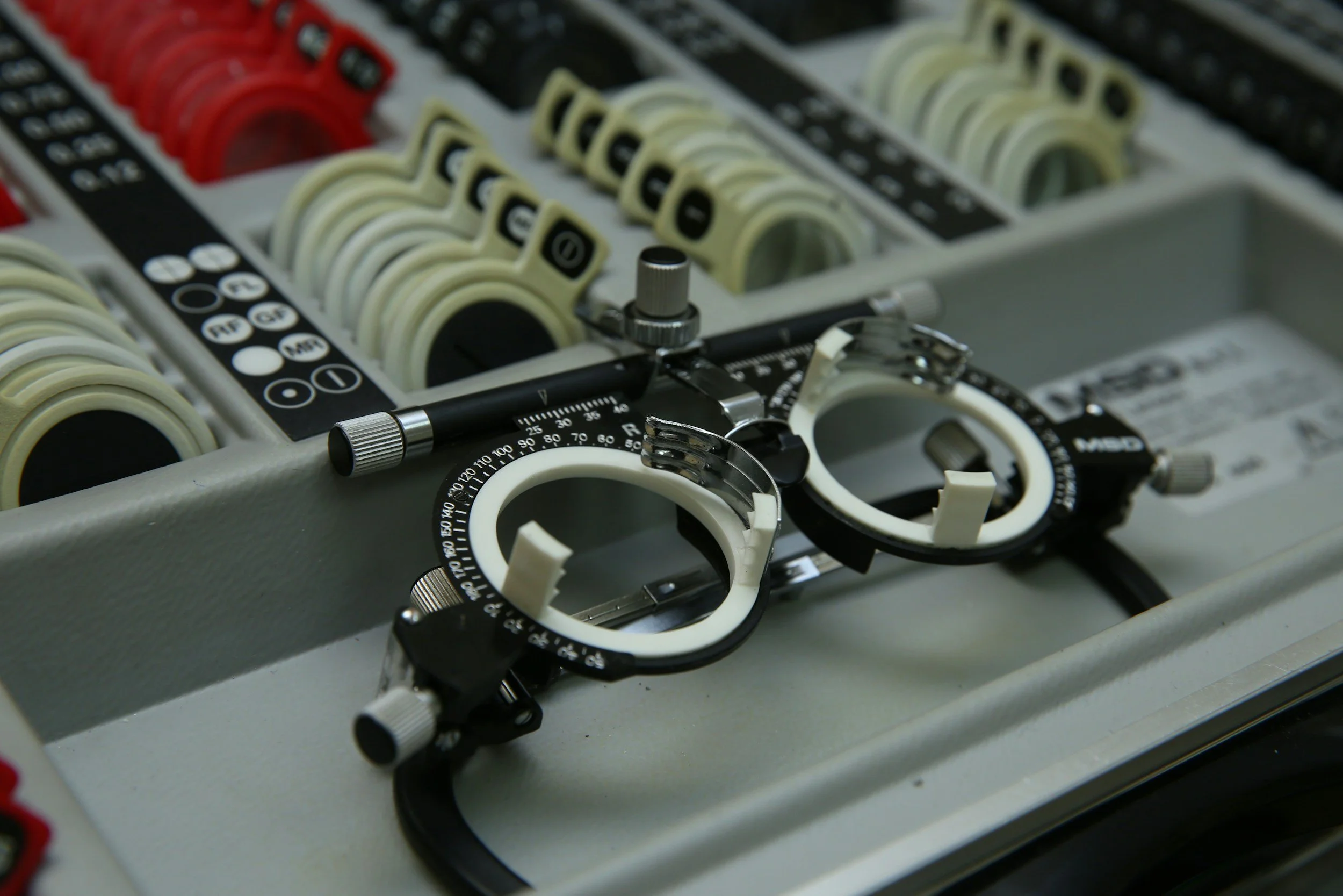 Close-up of an eye examination phoropter lens testing device with multiple dials and adjustable parts.