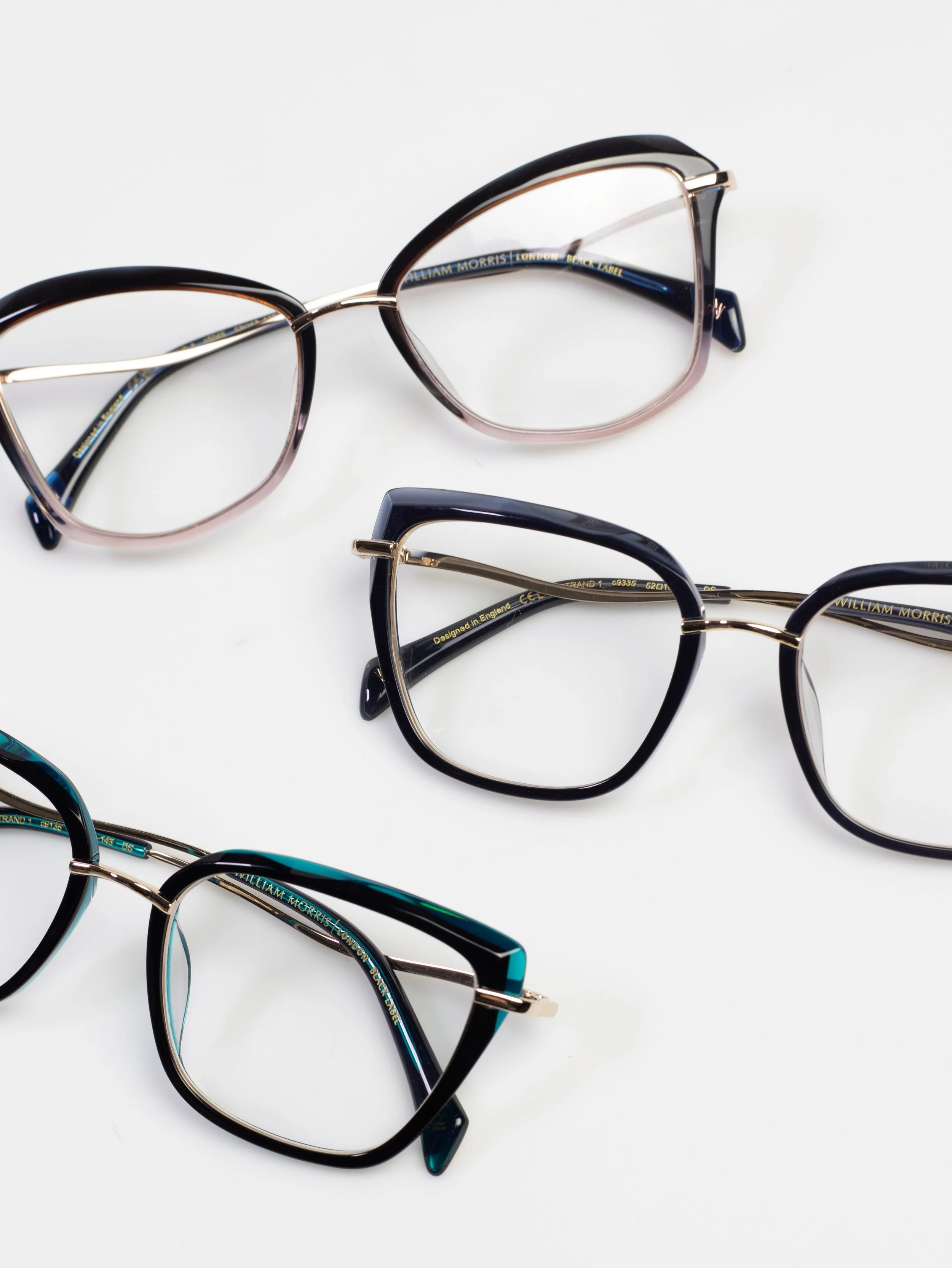 Multiple pairs of eyeglasses with different frame styles and colors arranged on a white surface.