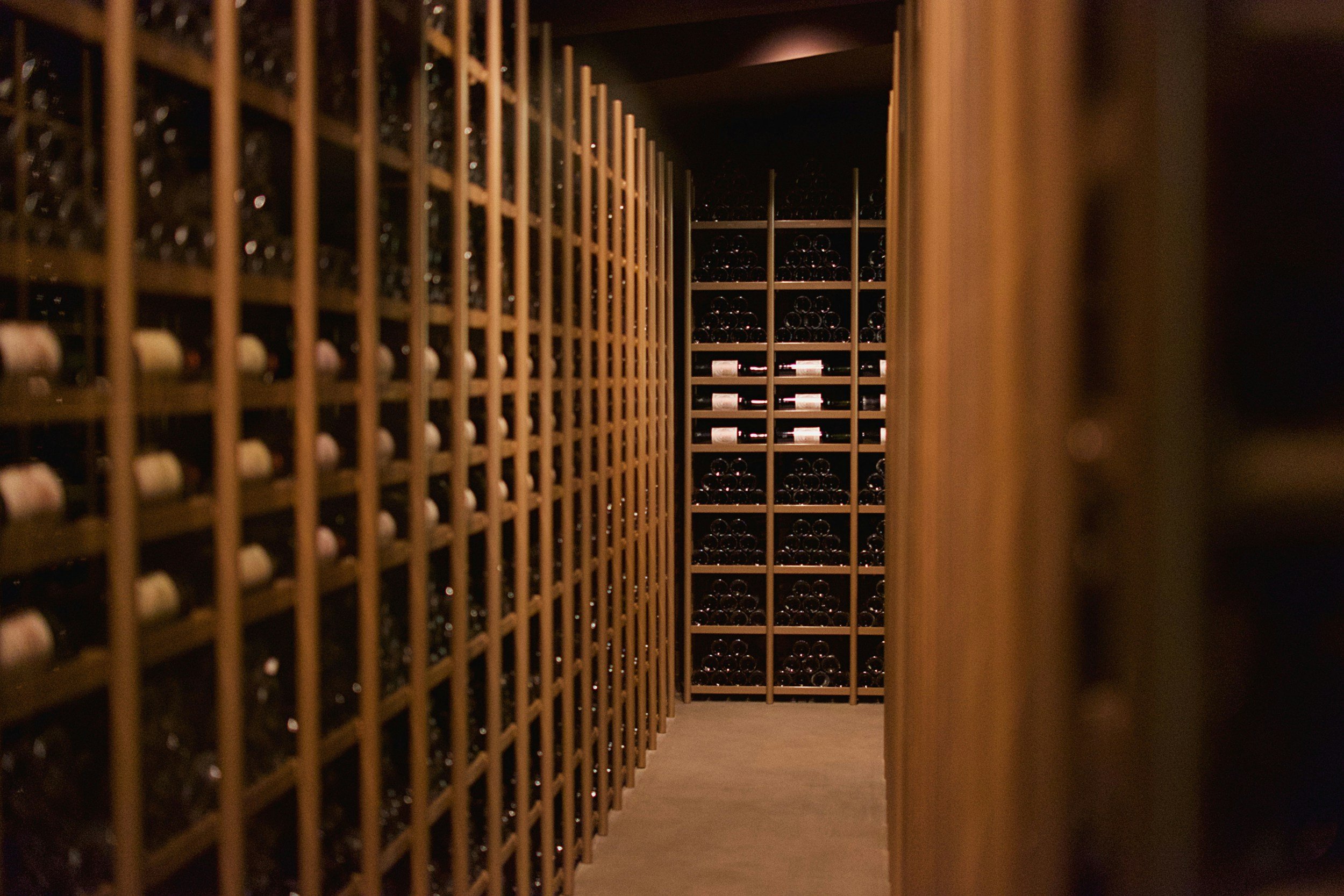 View of a wine cellar with wooden racks filled with wine bottles, seen through a narrow opening.