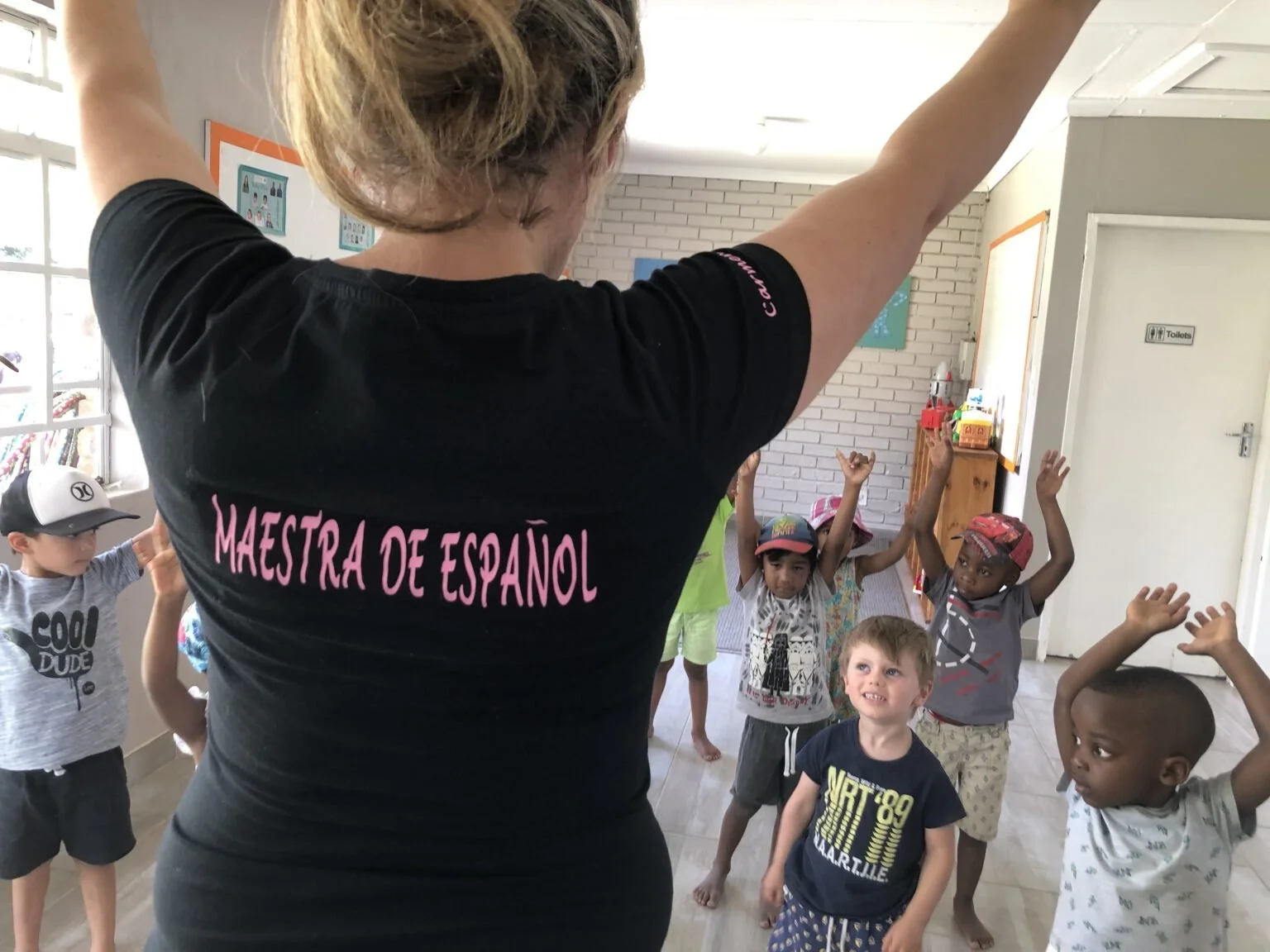 A woman leading a group of children in a physical activity or dance in a classroom setting.
