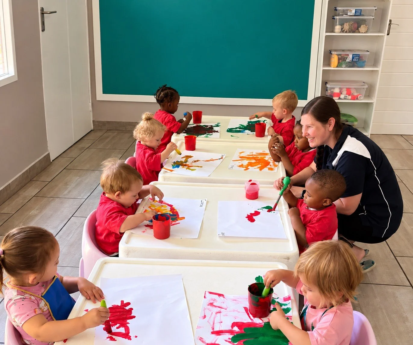 Children and their teacher in a classroom engaging in painting activities at a craft table.