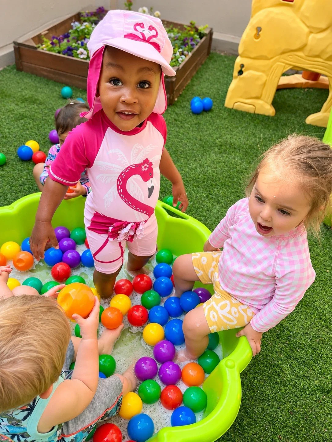Children playing in a plastic ball pit with colorful balls on green grass in an outdoor play area