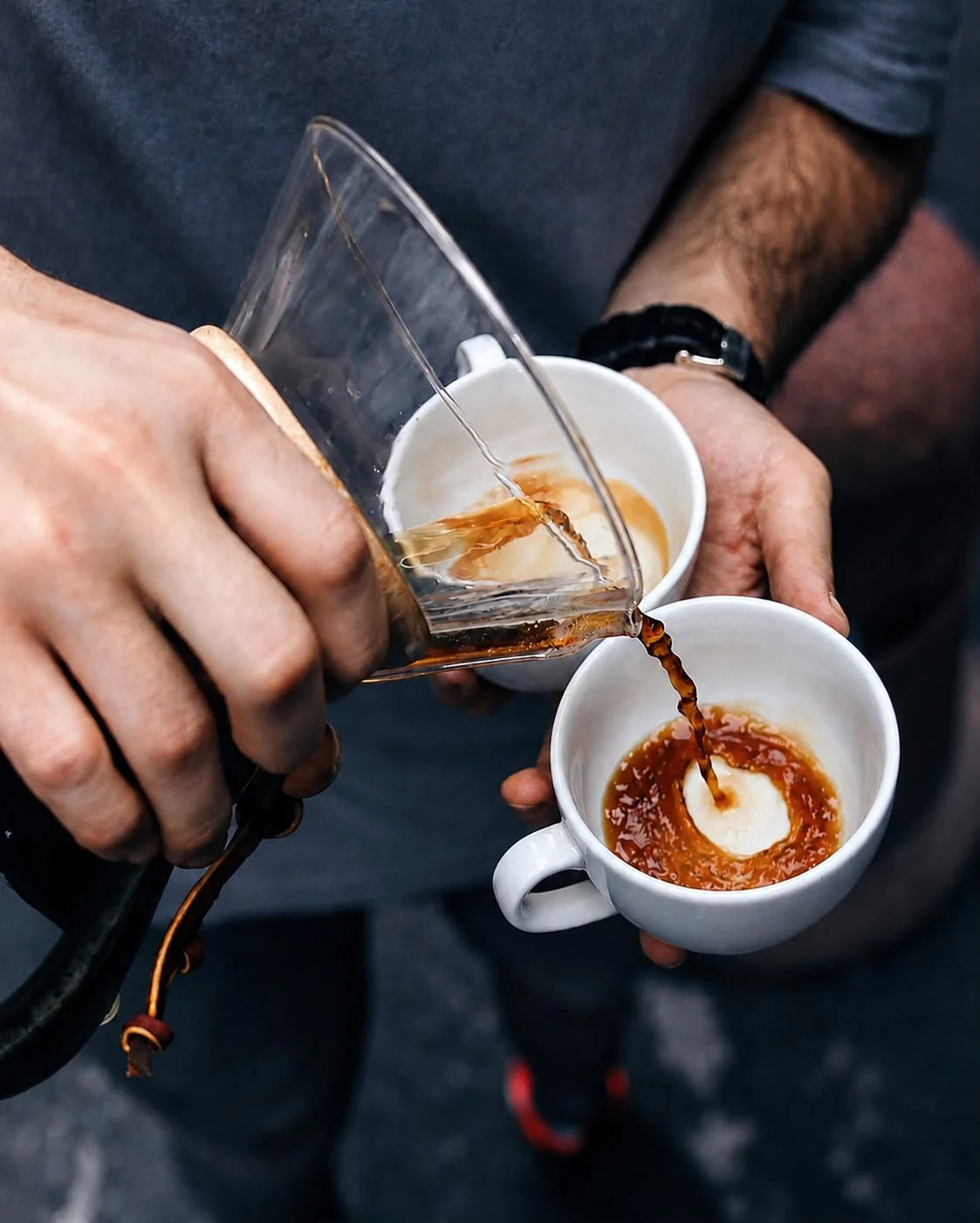Barista pouring hot coffee from a glass pot into two white ceramic cups for event. specialty coffee service at an event, serving freshly prepared coffee to guests.