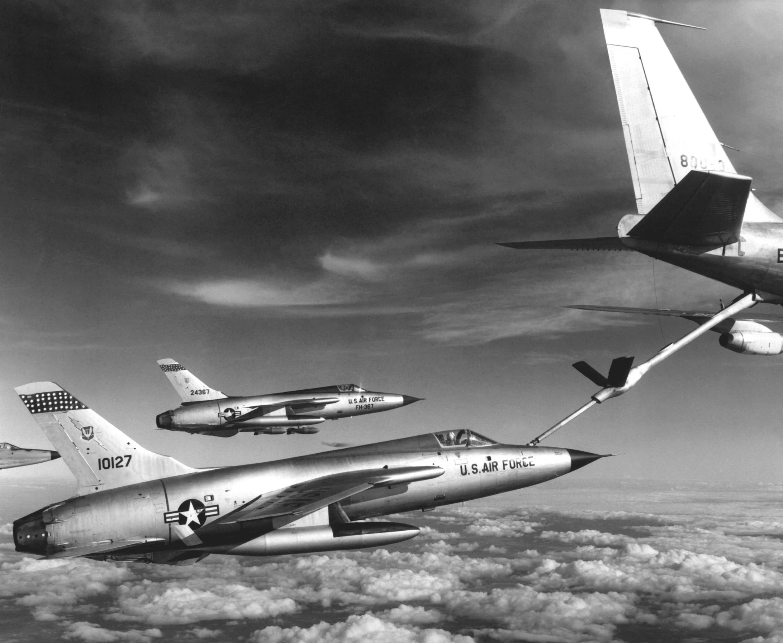 Black and white photo of multiple U.S. Air Force fighter jets flying in formation over the clouds.