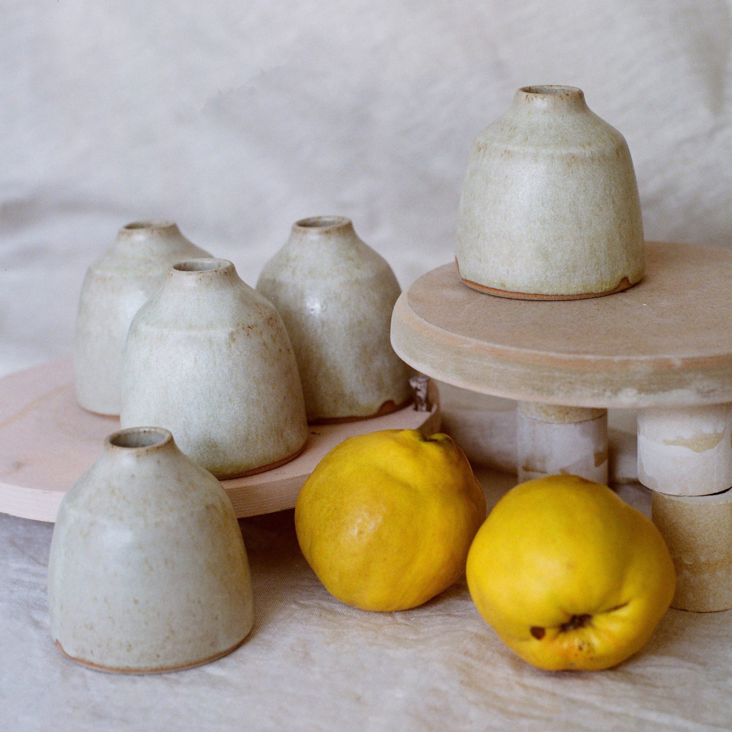 A collection of white and yellow ceramic vases and bowls on a white surface, with a white background. Citrus fruit for decoration in the foreground.