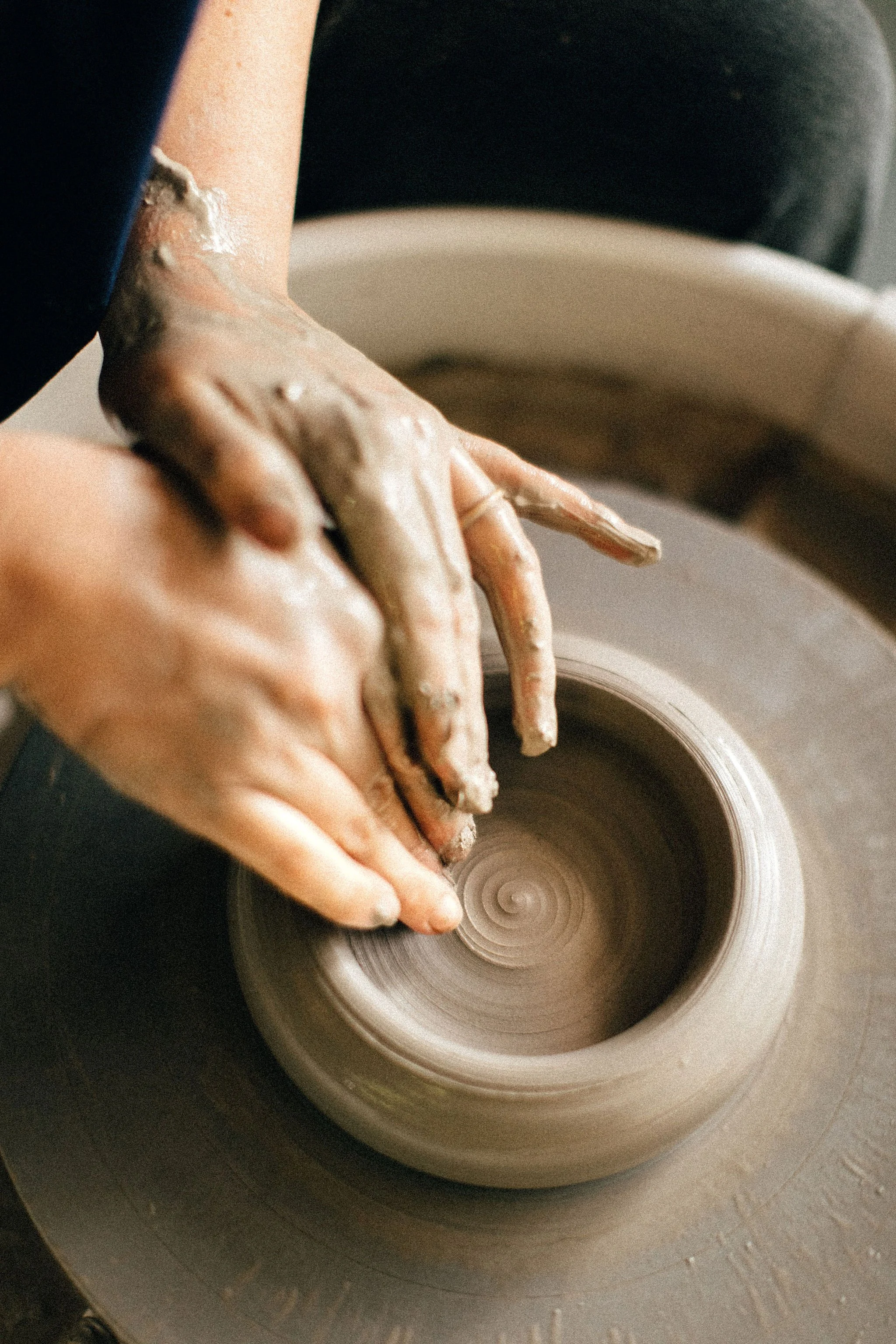 Hands shaping a clay pot on a spinning pottery wheel.