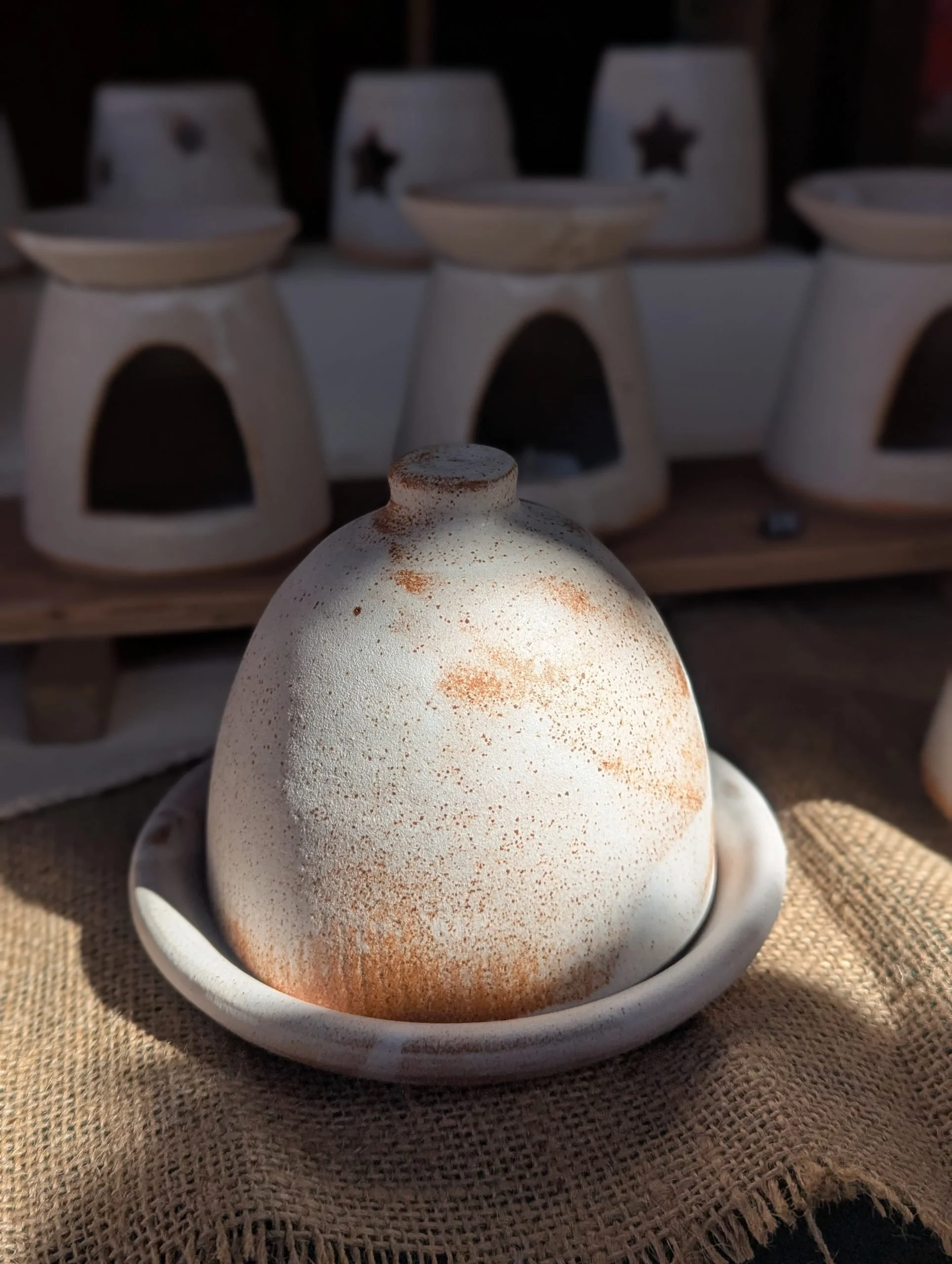 Close-up of a ceramic decorative object on a plate, with a shelf of ceramic houses in the background.