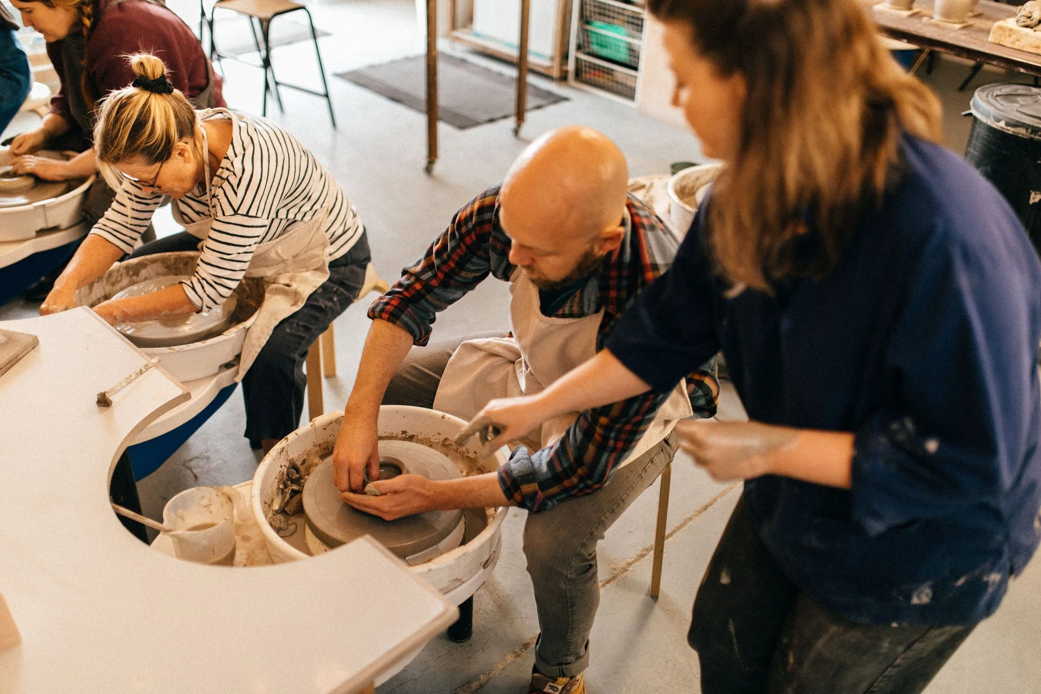 People working on pottery wheels in a pottery studio, shaping clay into pottery.