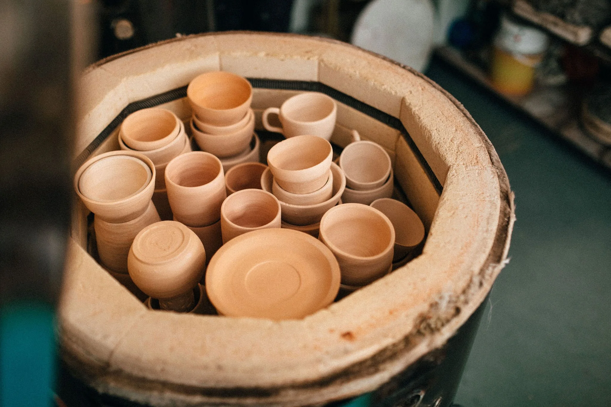 A close-up of a fully stacked pottery kiln with partially formed clay cups arranged inside it, in a ceramic workshop.