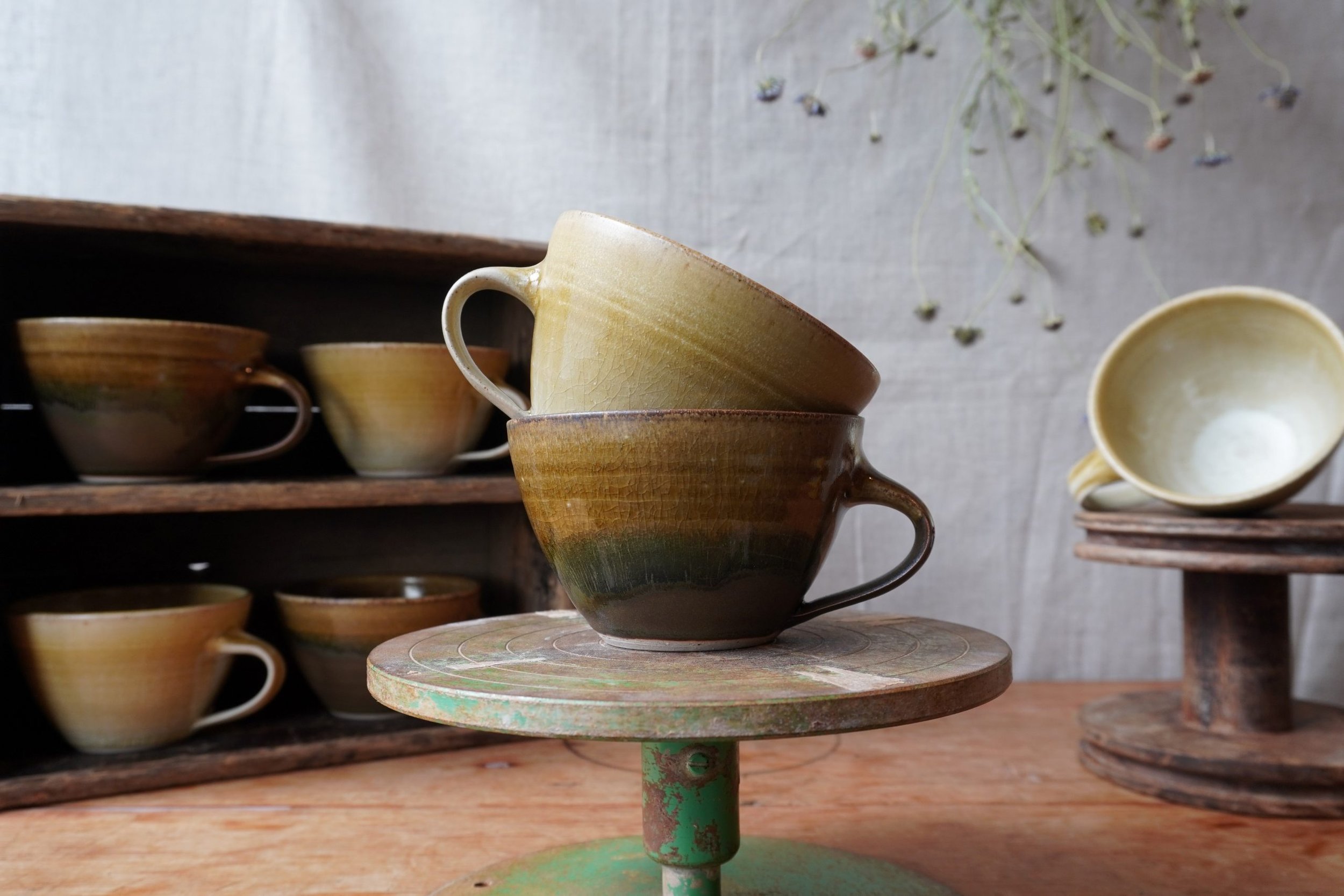 Stacked ceramic cups on a rustic shelf with a decorative stand in the foreground.
