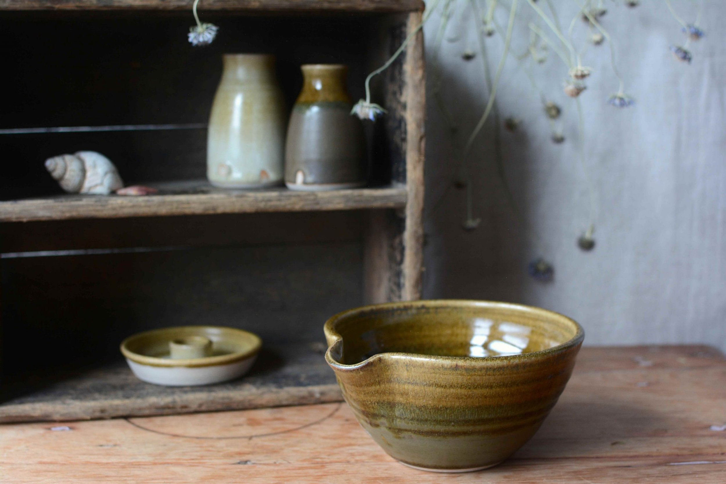 Close-up of pottery bowls and vases on a wooden shelf and table.